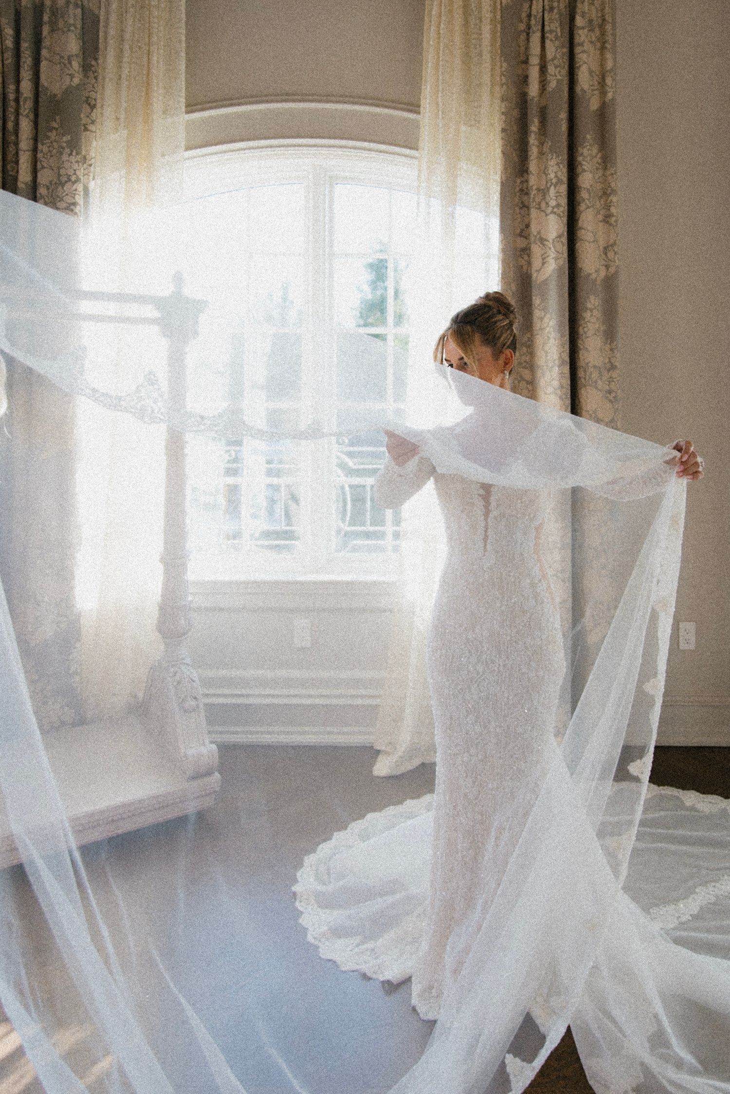 Ethereal white wedding dress and veil flowing gracefully in natural window light creating a dreamy atmosphere.
