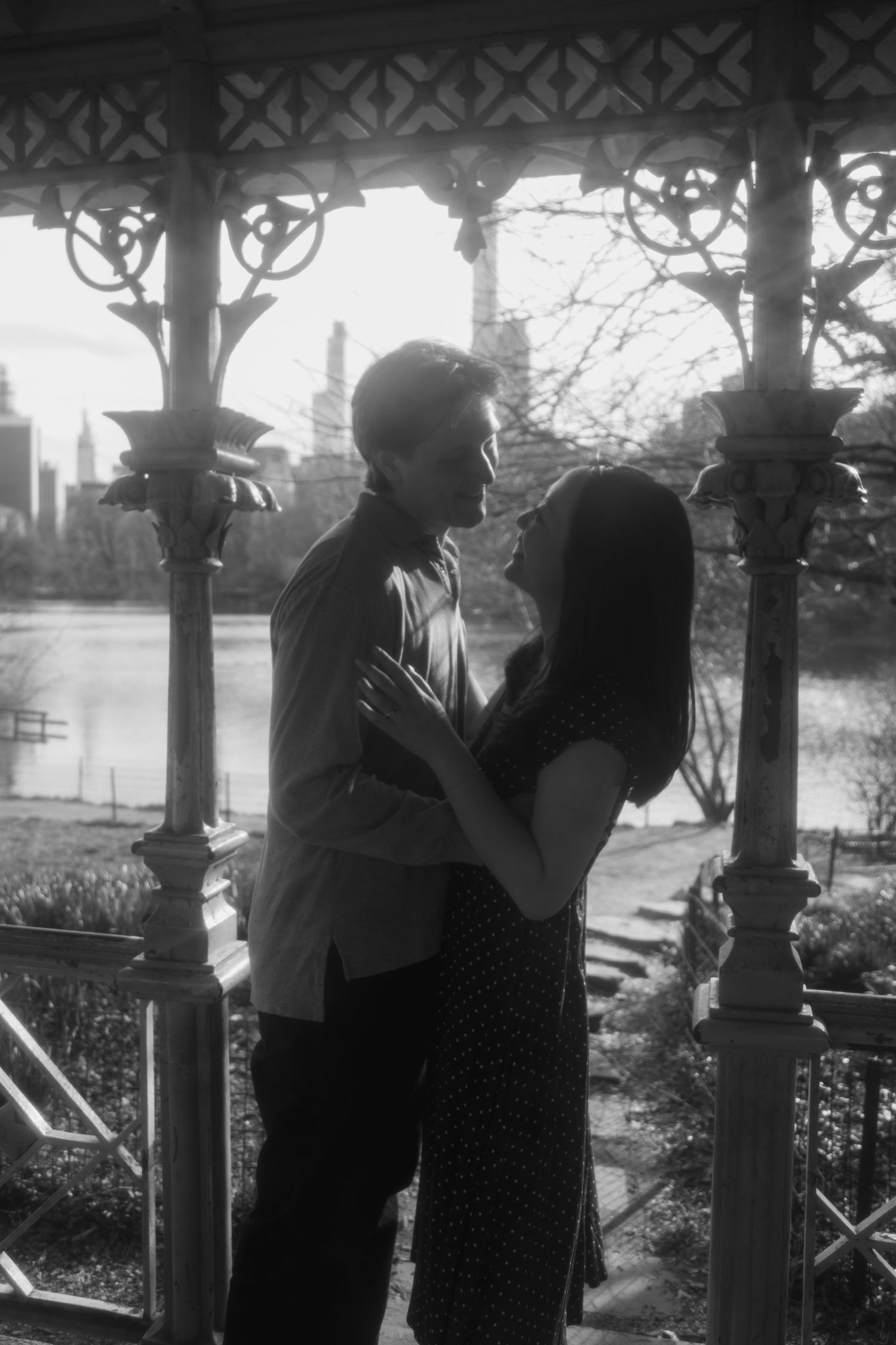 Two silhouetted figures against an ornate railing backdrop with sunlight filtering through trees.