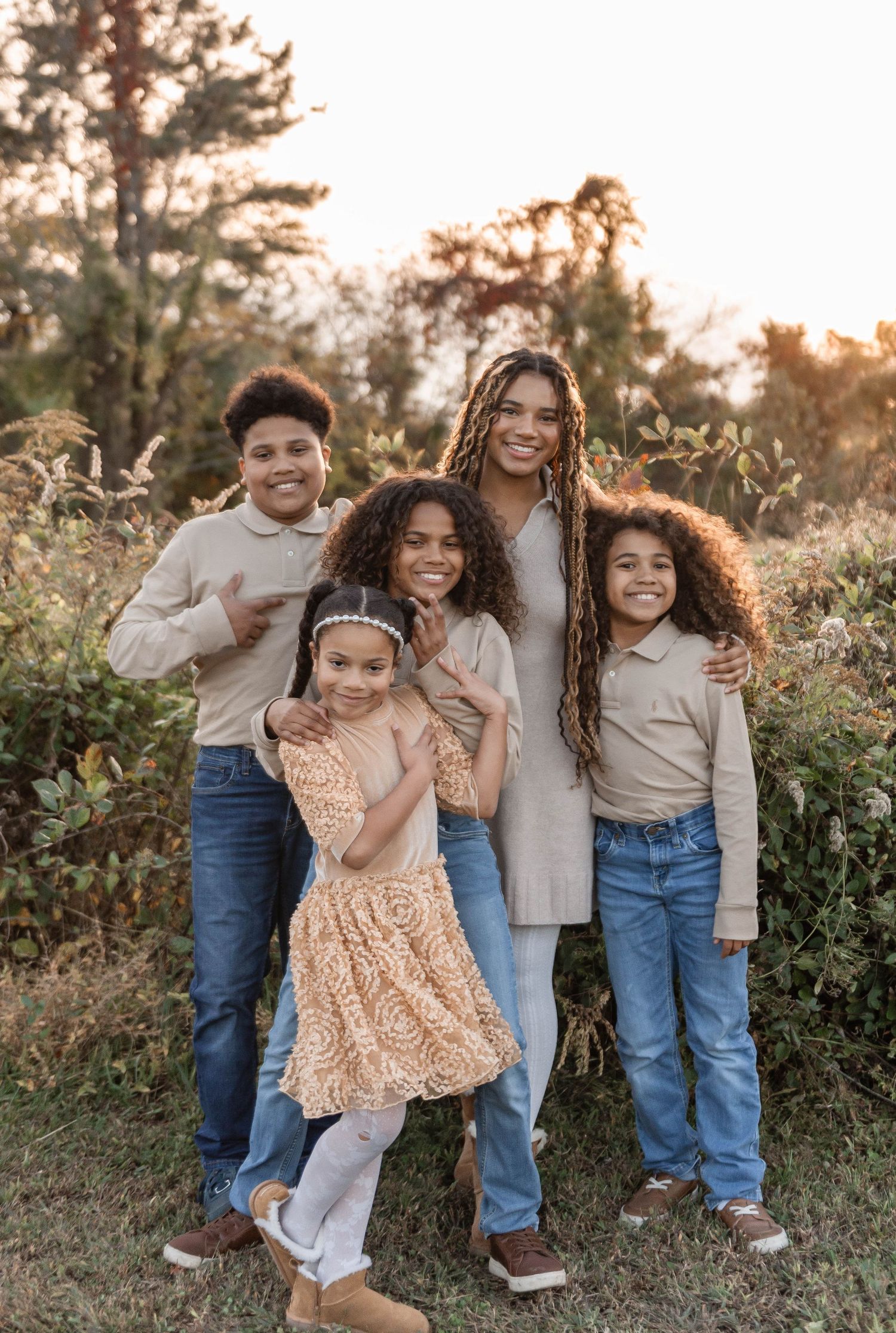 Mother with her four children smiling together in a sun-kissed outdoor fall setting.