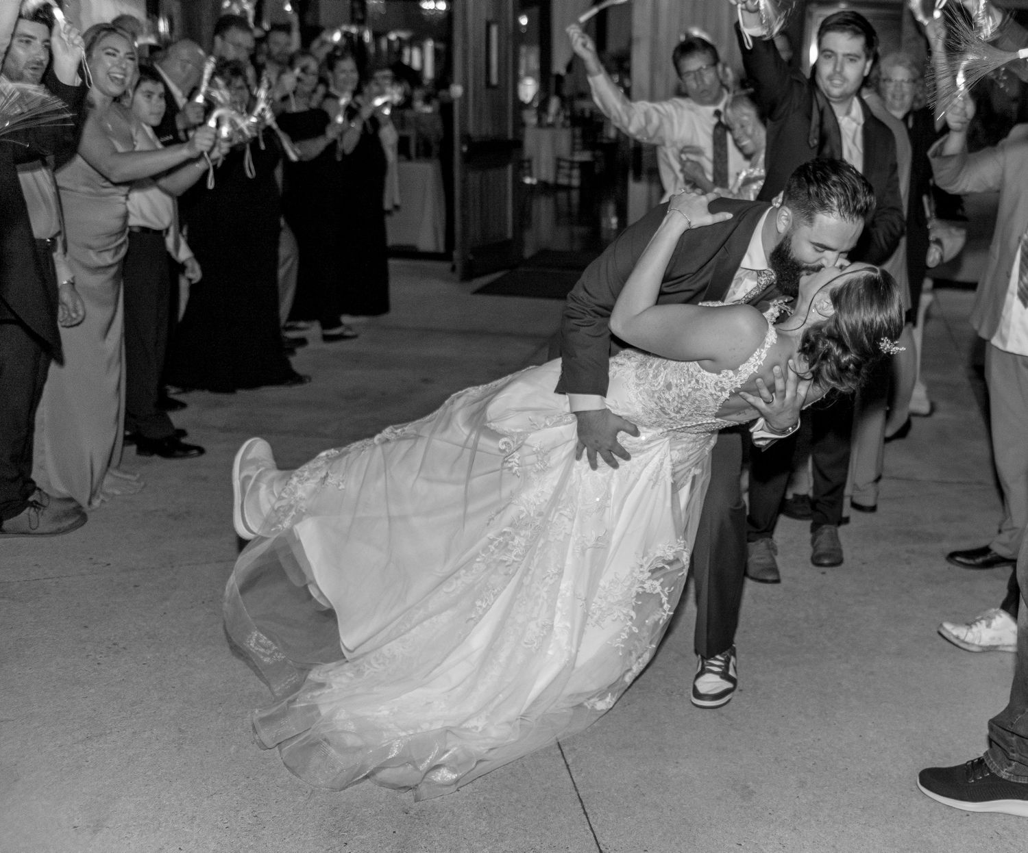 A groom dips his bride dramatically during a sparkler send-off exit in a black and white wedding photo.