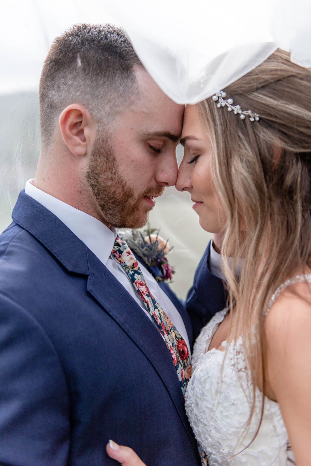 Bride and groom share an intimate forehead touch moment, groom in navy suit with floral tie.