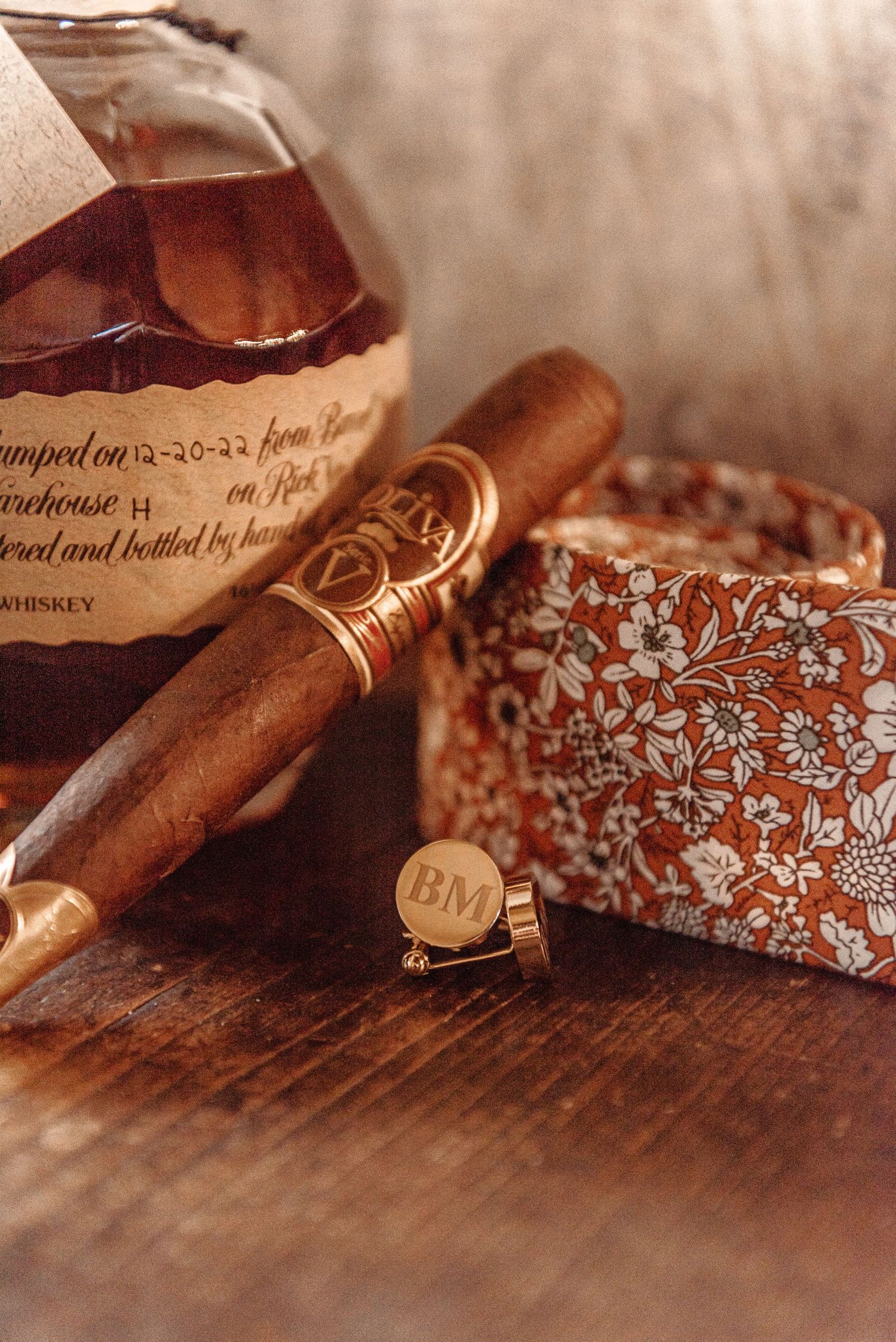 Personalized monogram cufflinks, cigar, and whiskey bottle styled as groom wedding day details.