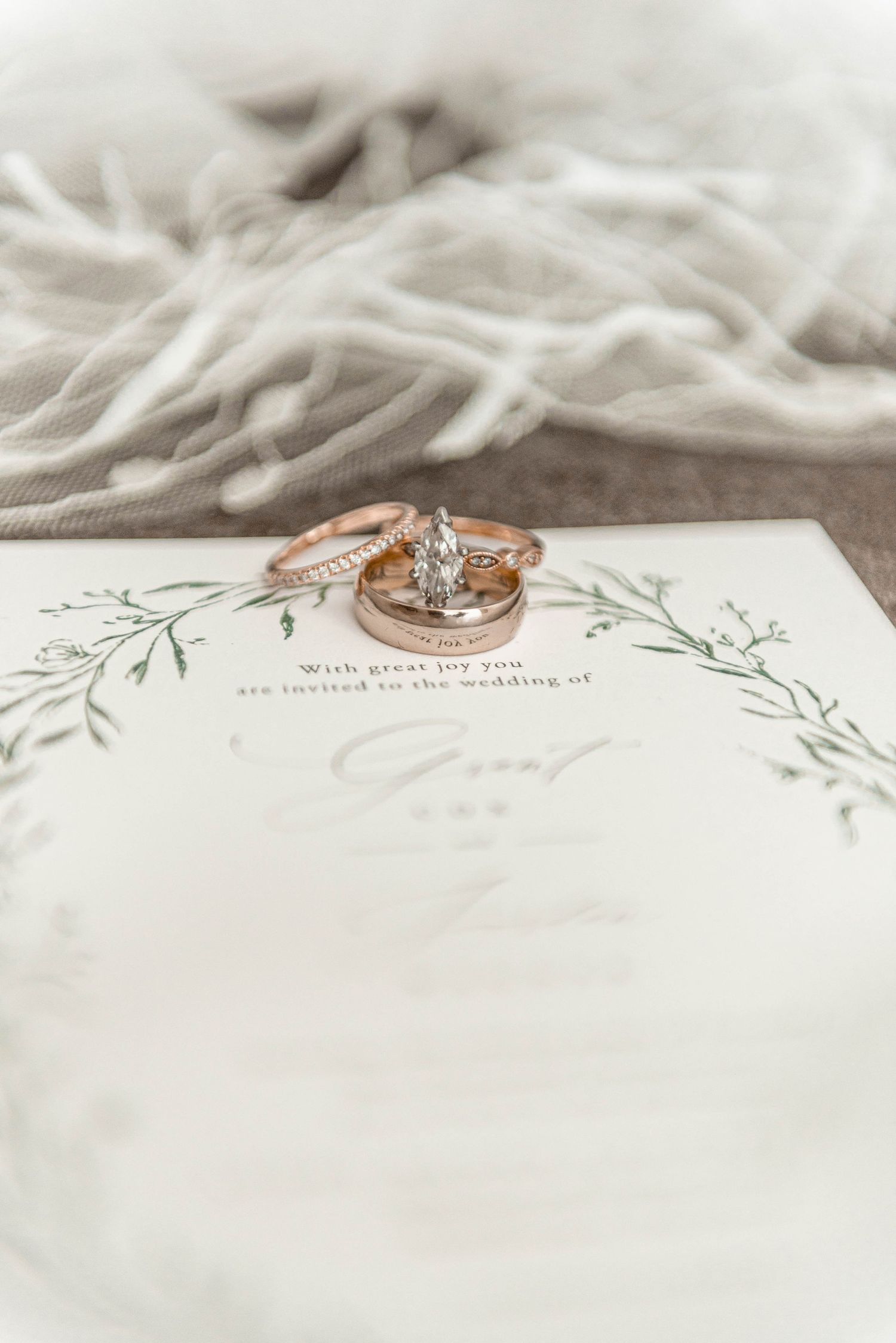 Rose gold wedding rings and diamond engagement ring displayed on elegant floral wedding invitation.