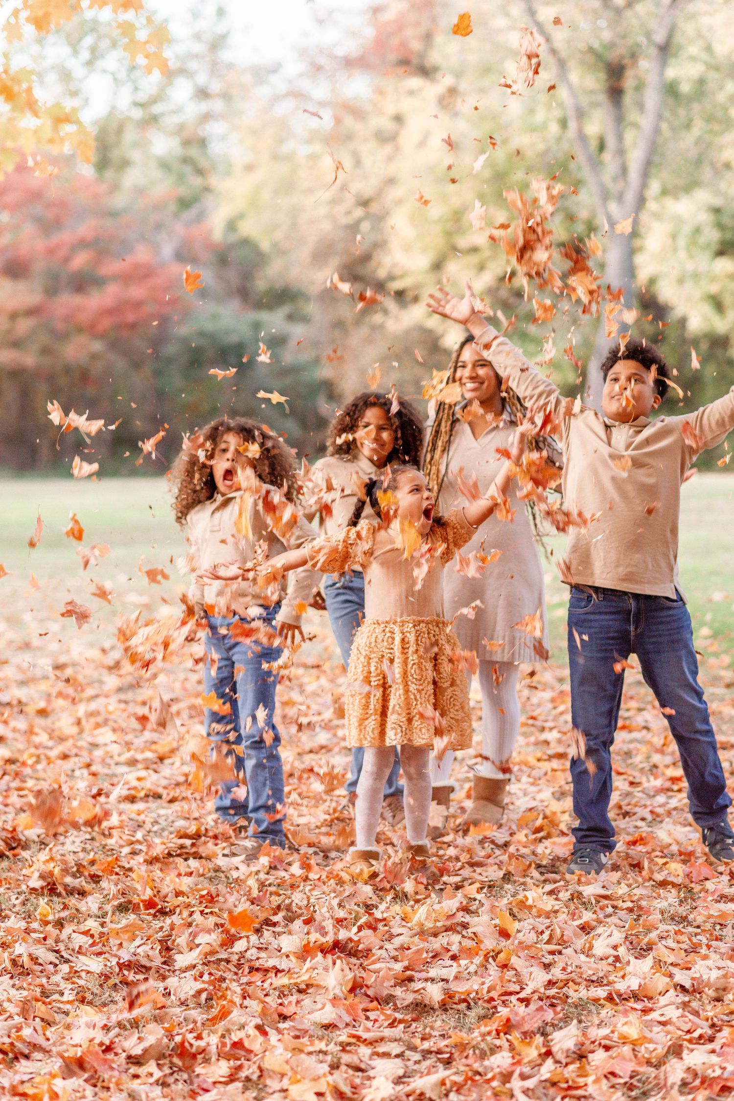 A joyful family tossing golden autumn leaves in the air outdoors during a vibrant fall season.