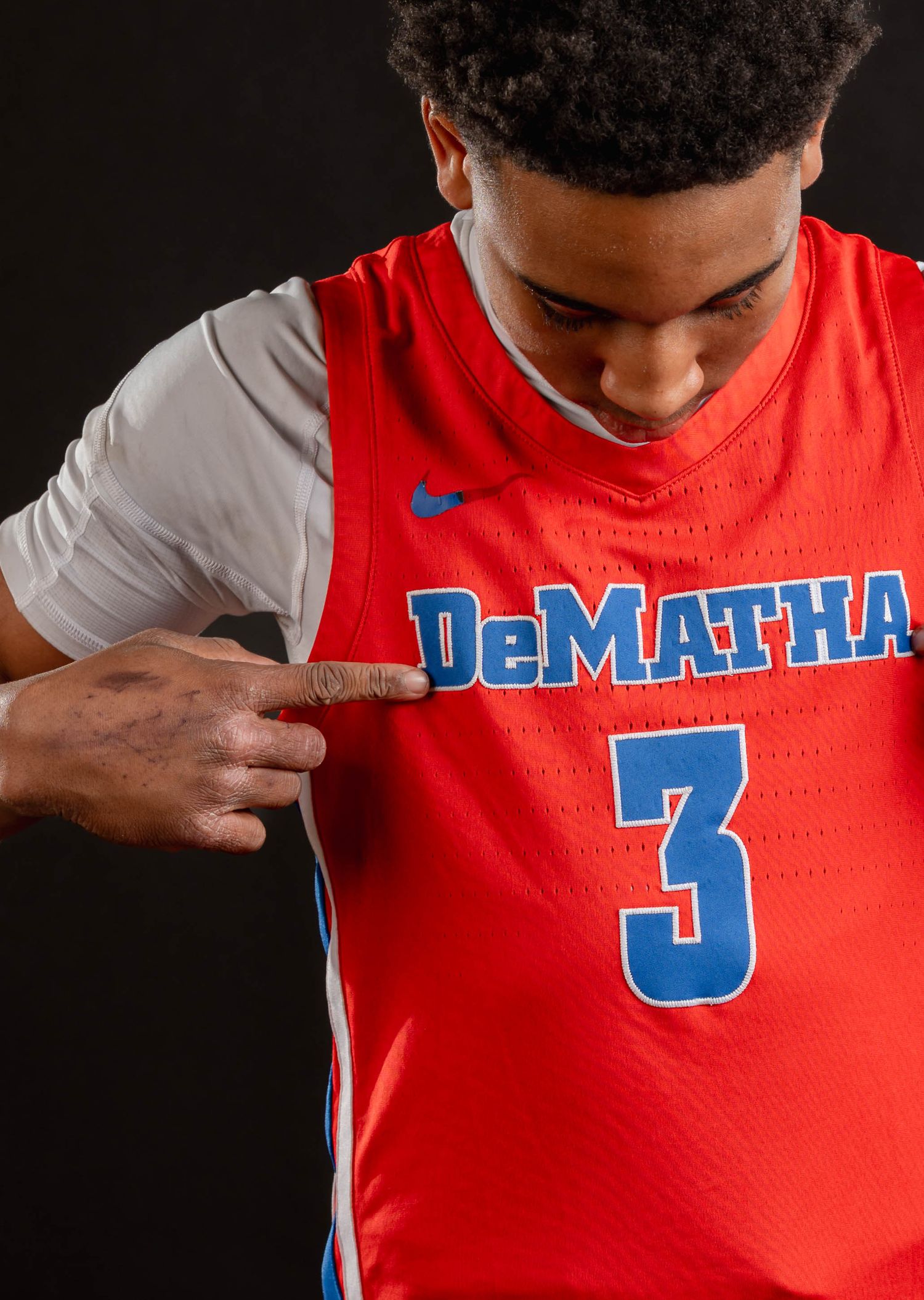 Basketball player points to DeMatha #3 jersey in close-up studio portrait.