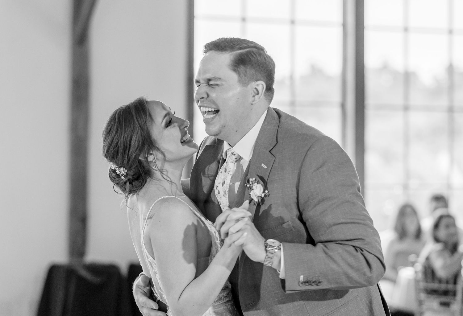 Black and white photo of laughing bride and groom sharing joyful first dance at wedding reception.
