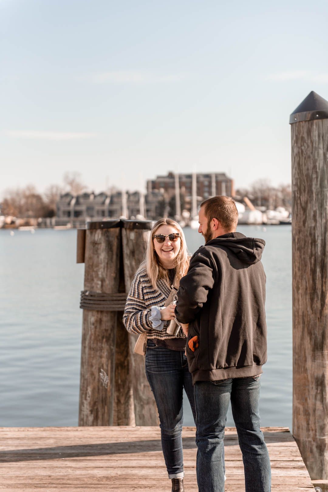 Smiling woman in striped sweater and sunglasses talking with man on a sunny marina dock.