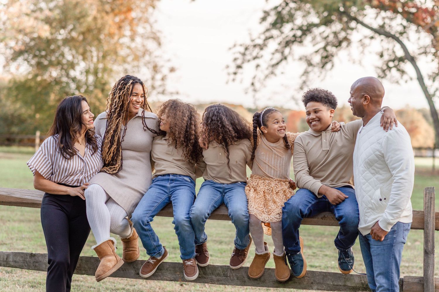 Joyful family of six sitting on fence laughing together during outdoor fall family portrait session.