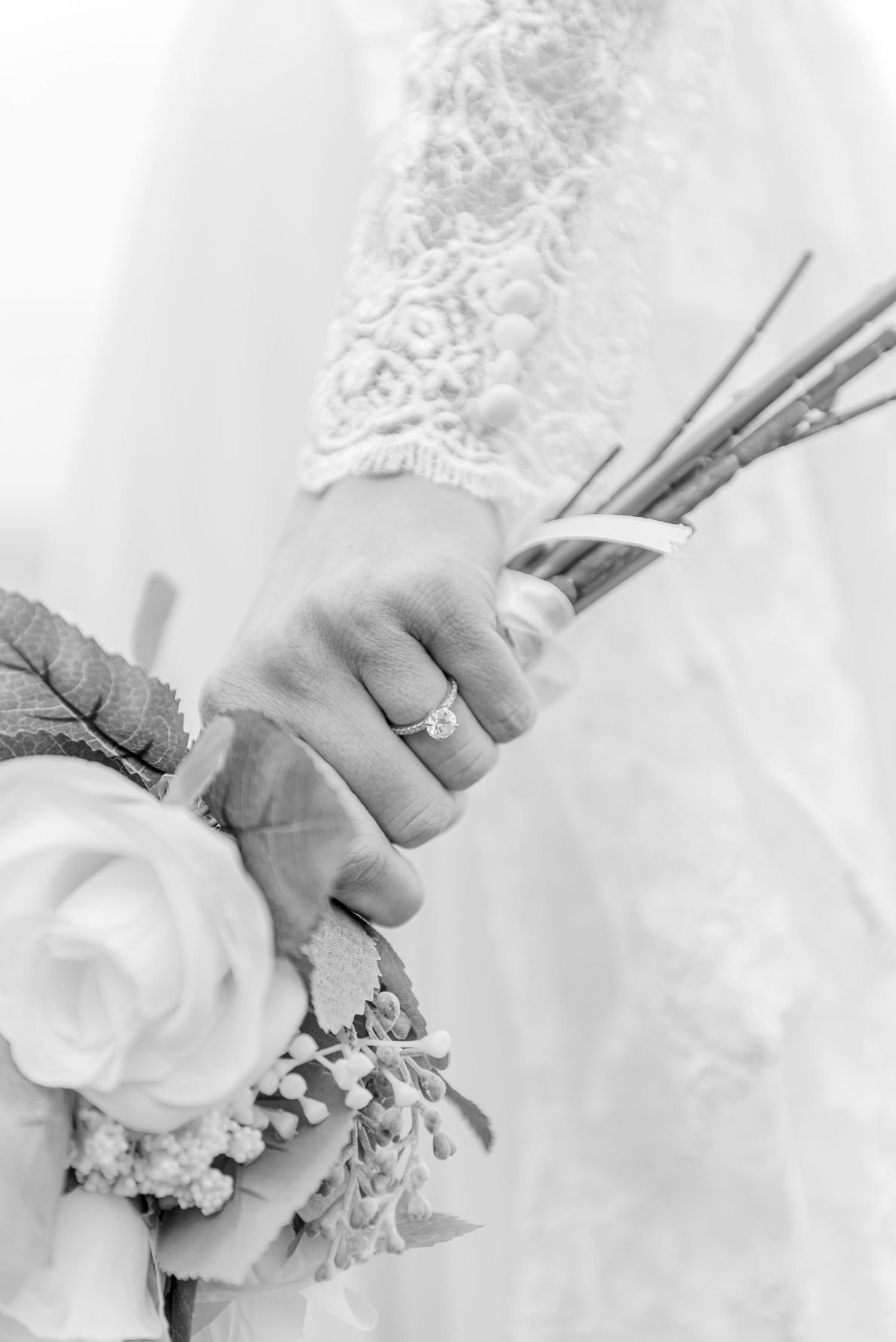 Black and white close-up of bride holding bouquet with diamond engagement ring.
