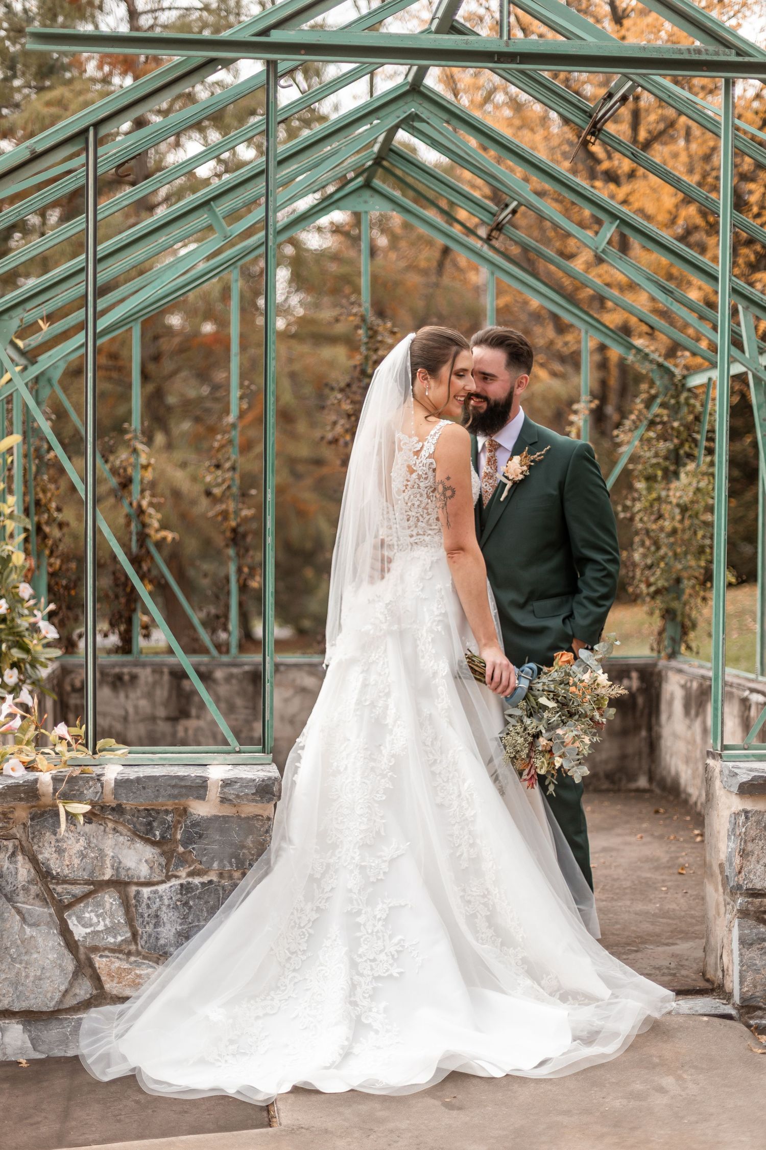 Bride and groom embrace before vintage greenhouse in autumn wedding portrait.