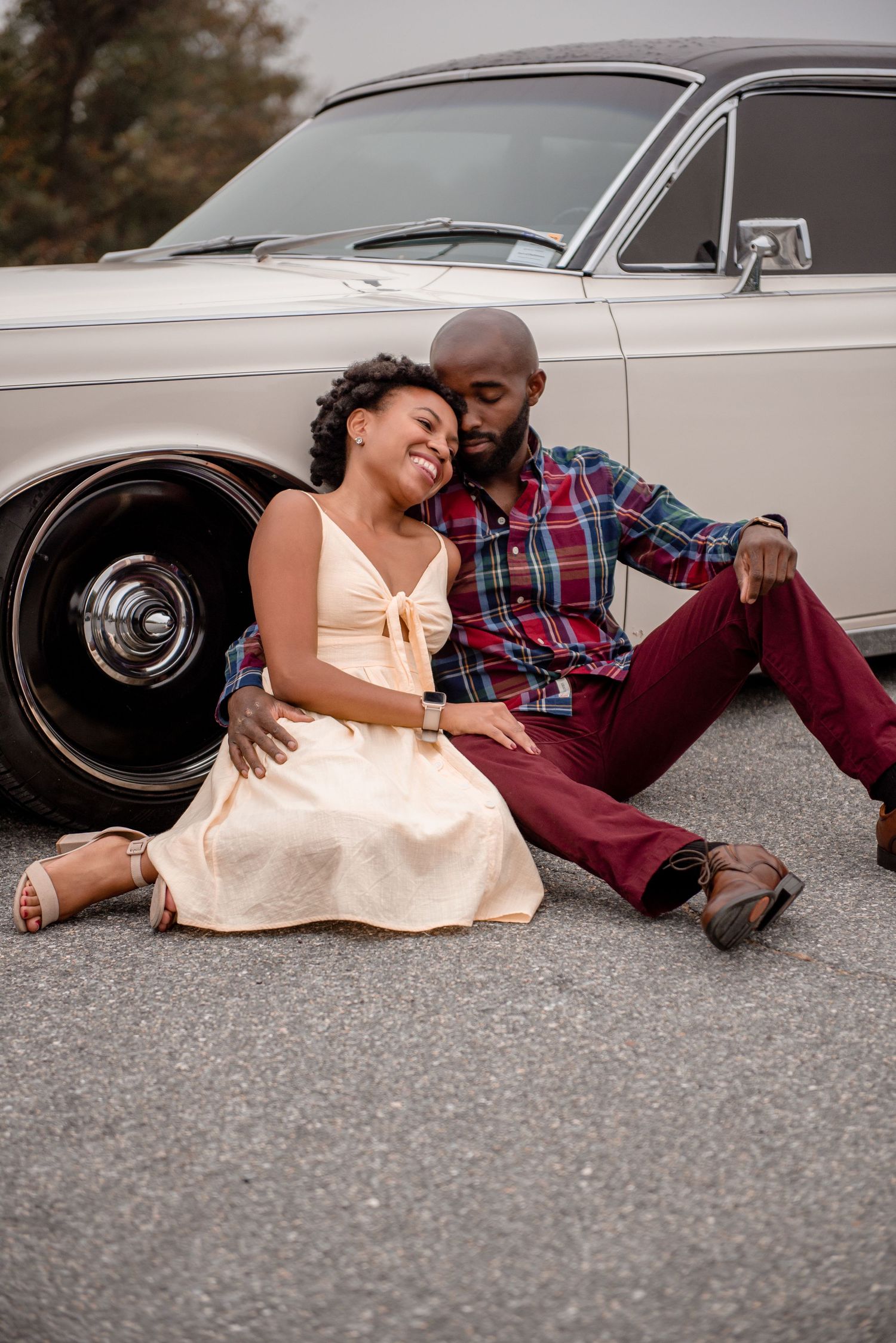 A couple relaxes on the ground against a classic white vintage car wheel in a romantic outdoor portrait.