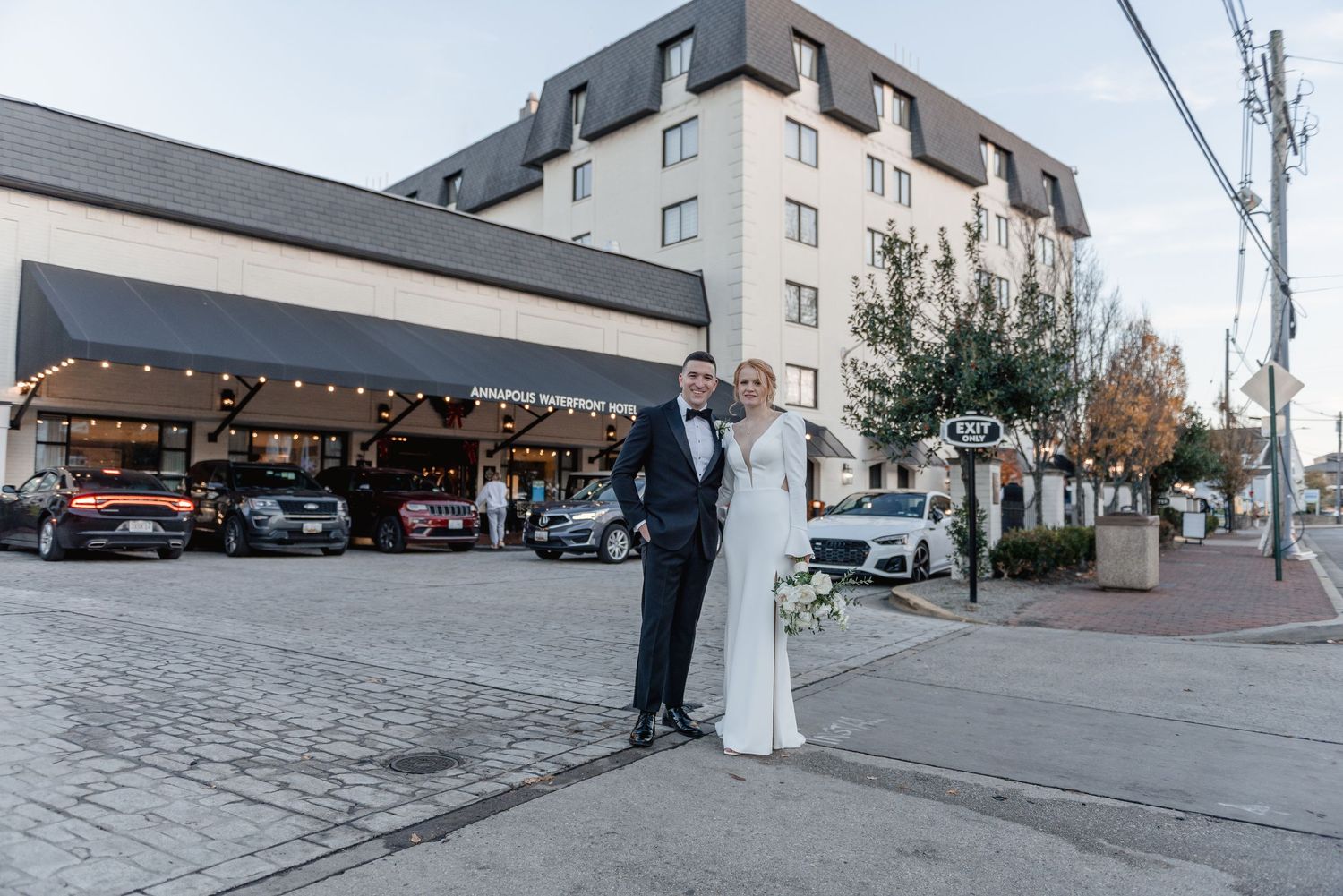 Bride and groom stand together on a city sidewalk with a hotel backdrop at their autumn wedding.