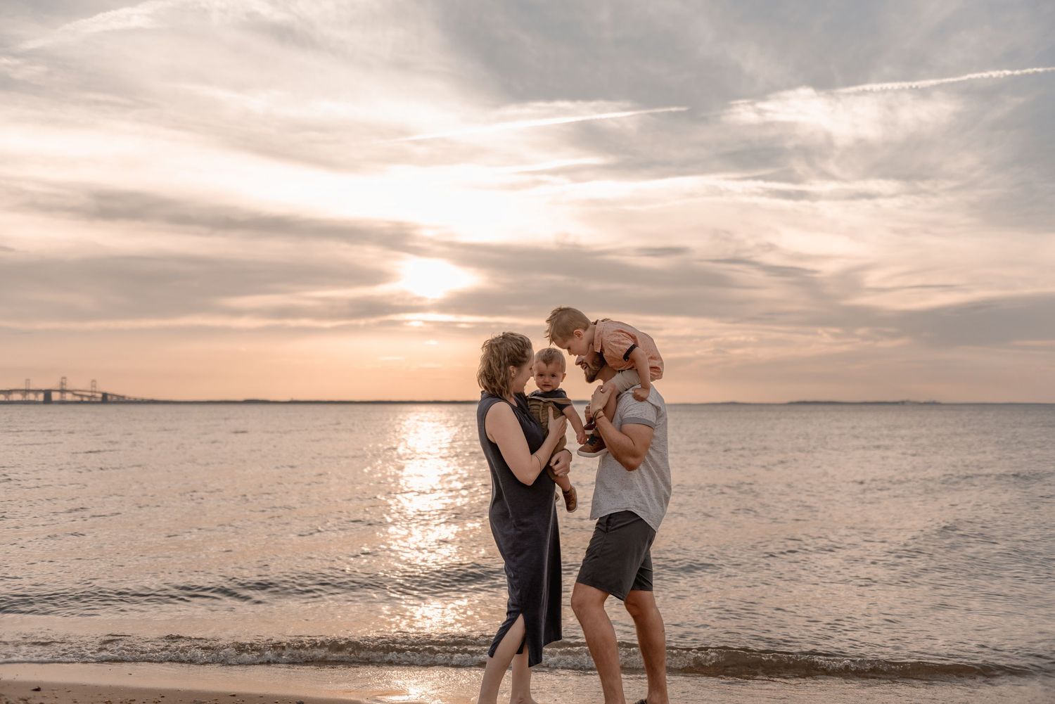 A family of four shares a joyful moment together on a sandy beach during a stunning sunset.