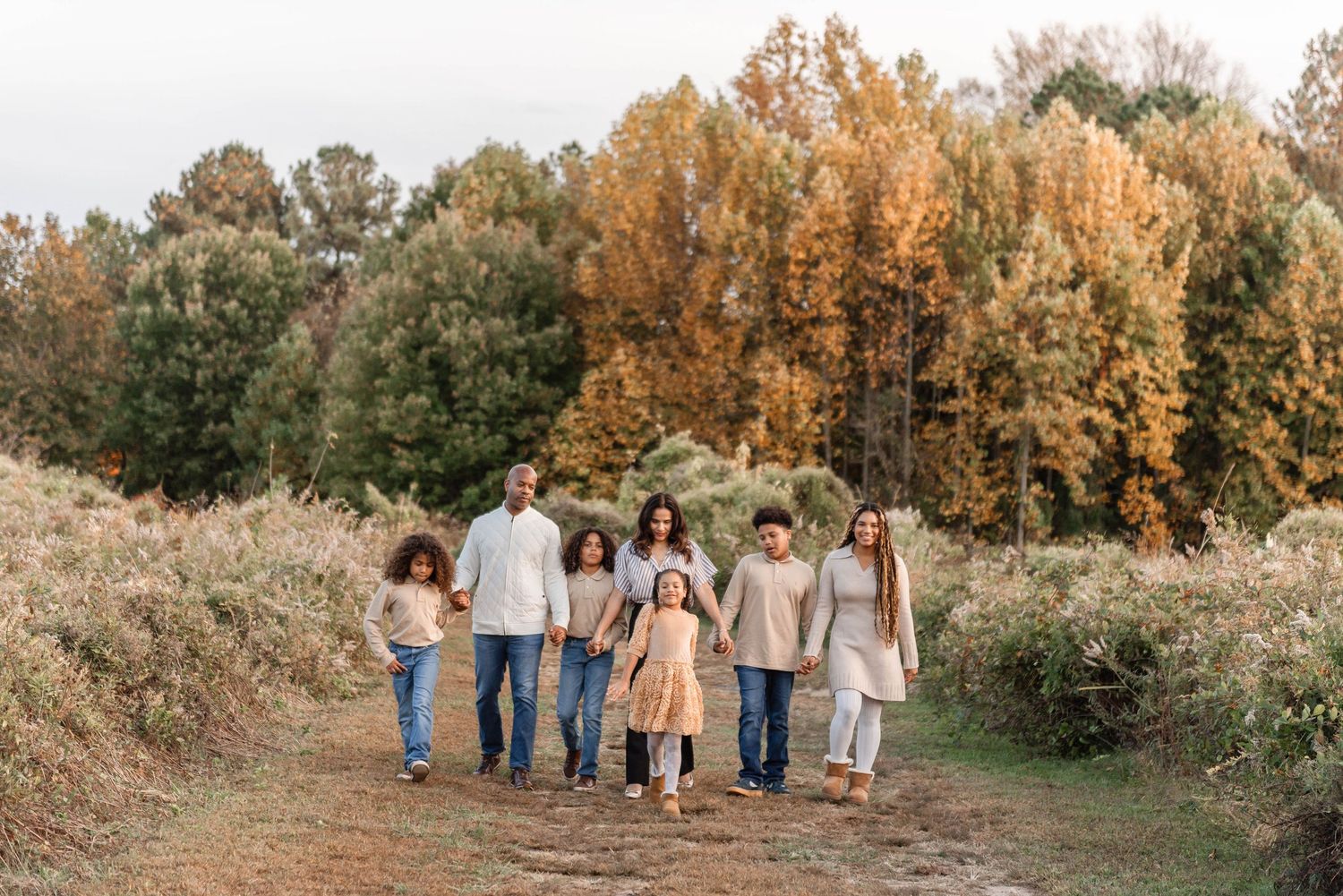 Family of seven walking hand-in-hand on a dirt path surrounded by vibrant autumn foliage.
