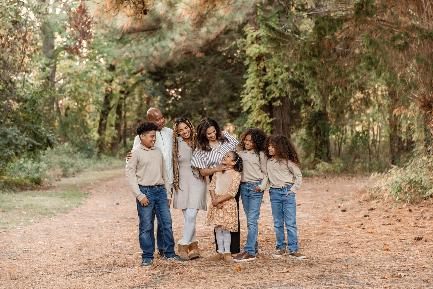 A loving family of seven laughing and embracing on a rustic dirt path surrounded by lush autumn trees.