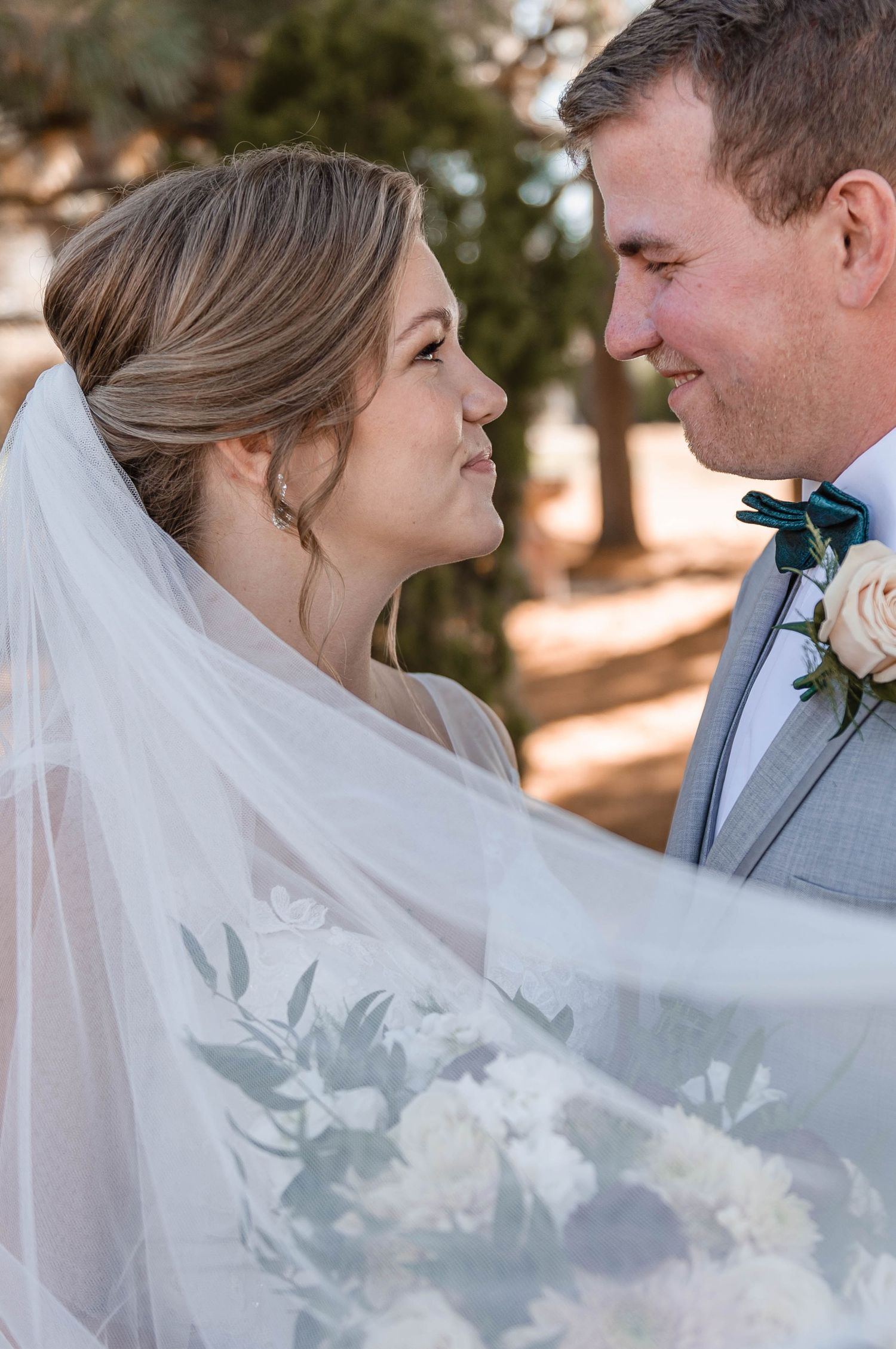 Bride and groom gaze lovingly at each other as her veil flows gently in the breeze outdoors.
