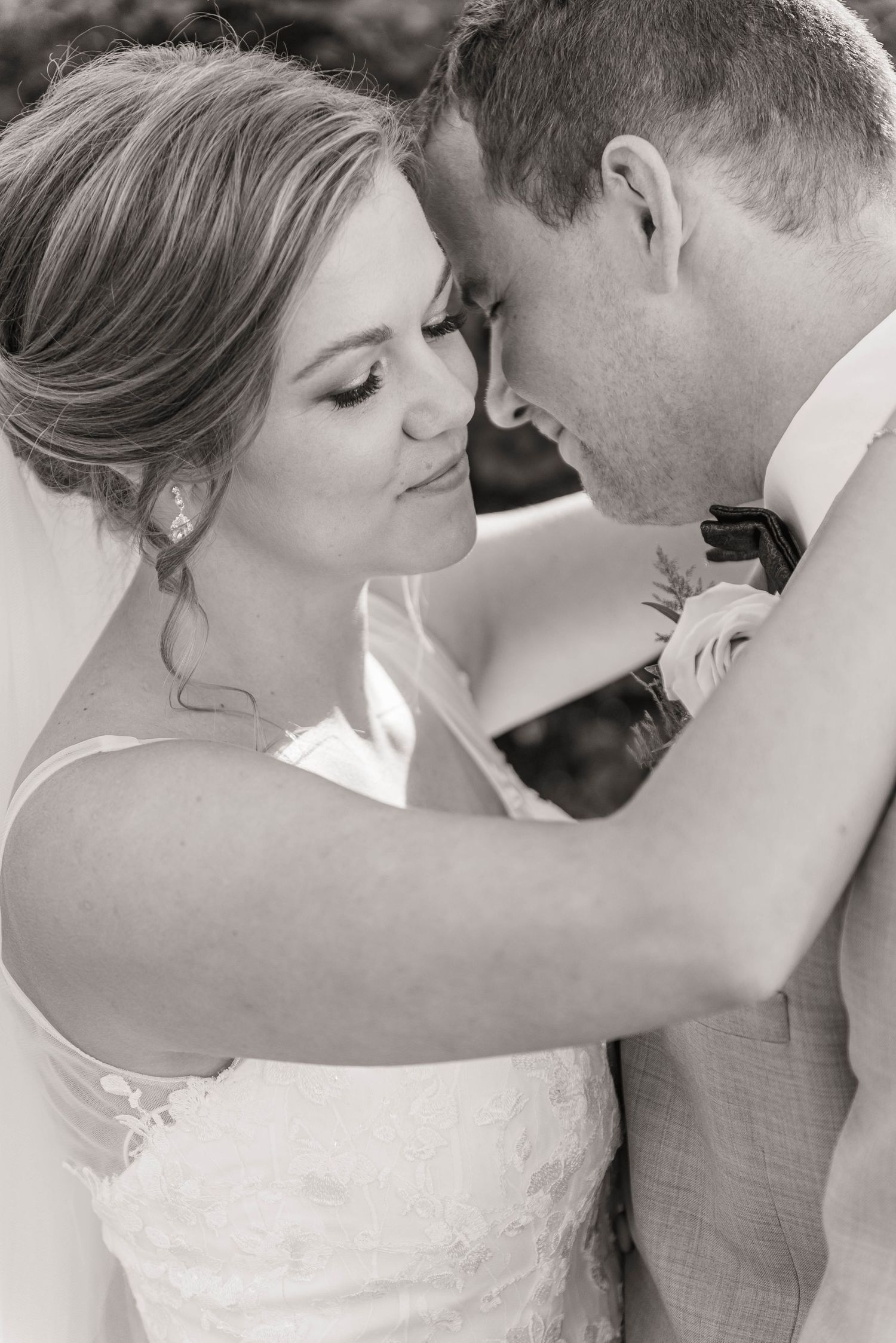 Black and white romantic portrait of bride and groom touching foreheads tenderly.