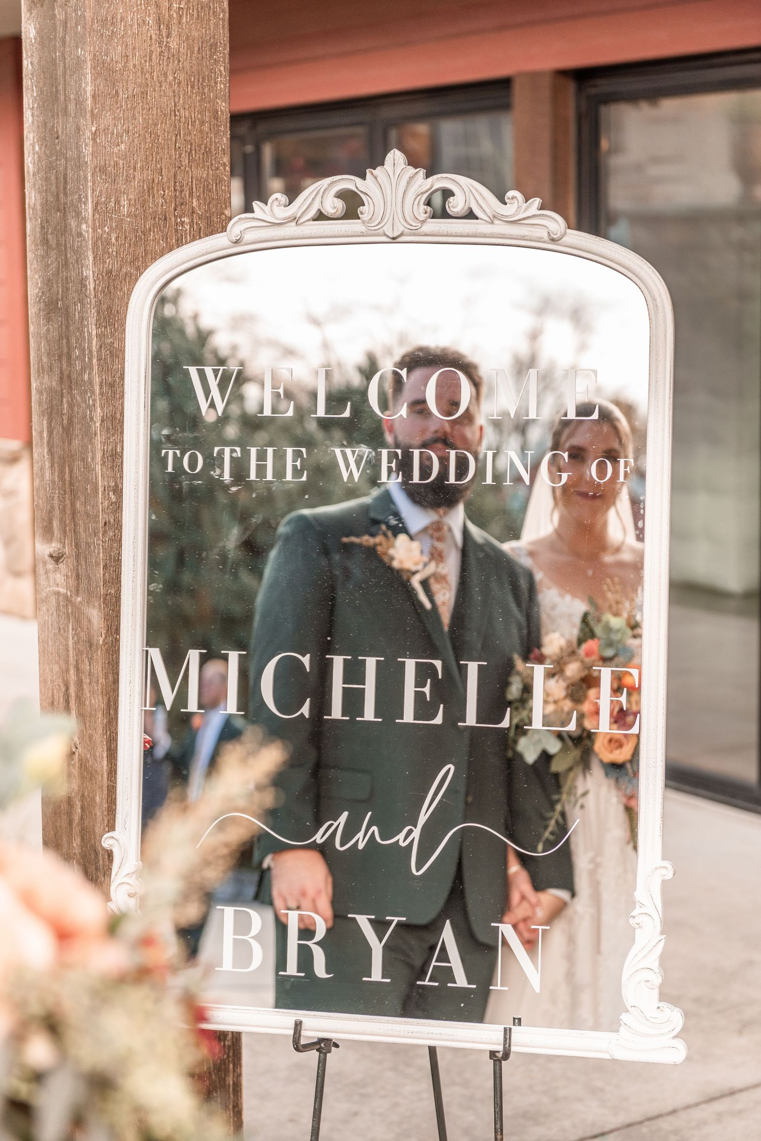 Welcome wedding mirror sign for Michelle and Bryan displayed on easel outside rustic venue entrance.