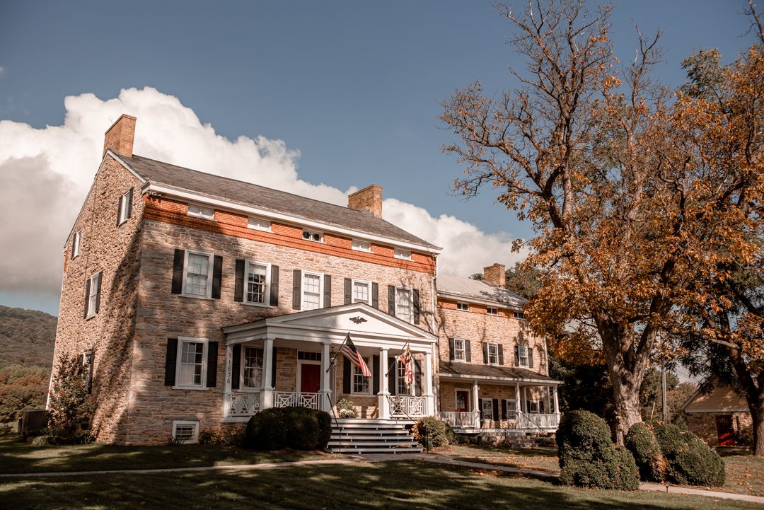 Historic brick colonial mansion wedding venue surrounded by autumn trees under dramatic cloudy sky.
