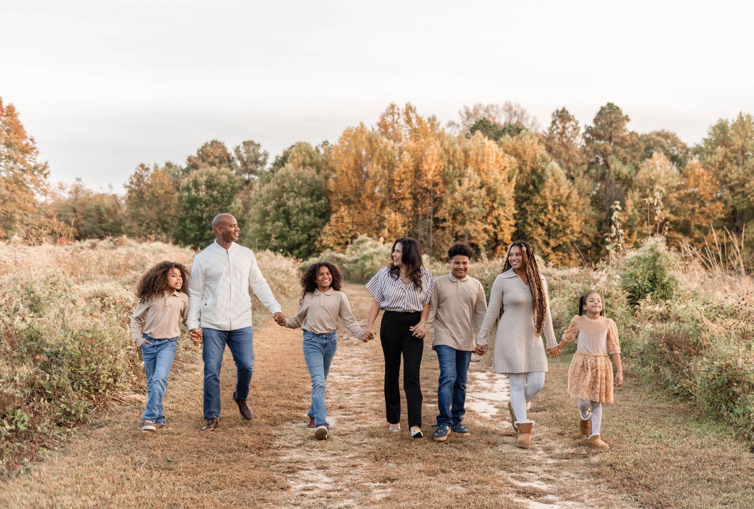 Family of seven strolling hand-in-hand along a scenic path with colorful fall trees.