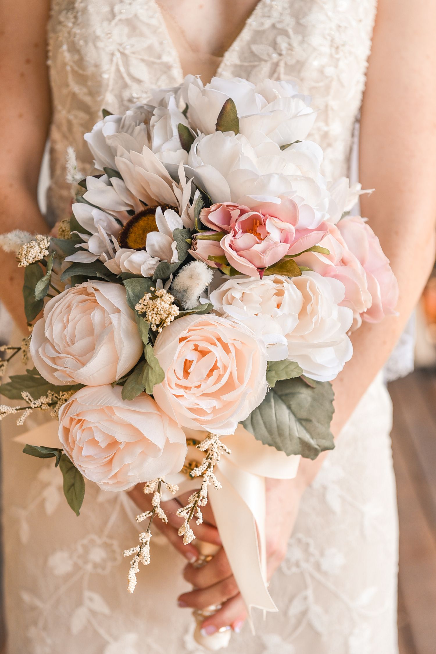 Bride holding a romantic bouquet of blush pink and white peonies with greenery, wearing a lace wedding gown.