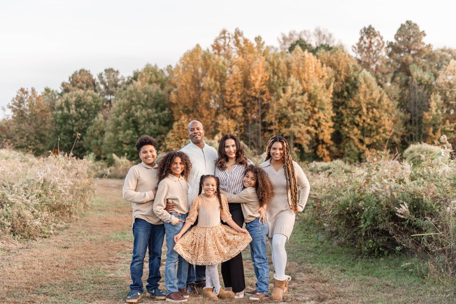 Family of seven posing together on a dirt path surrounded by vibrant fall foliage.
