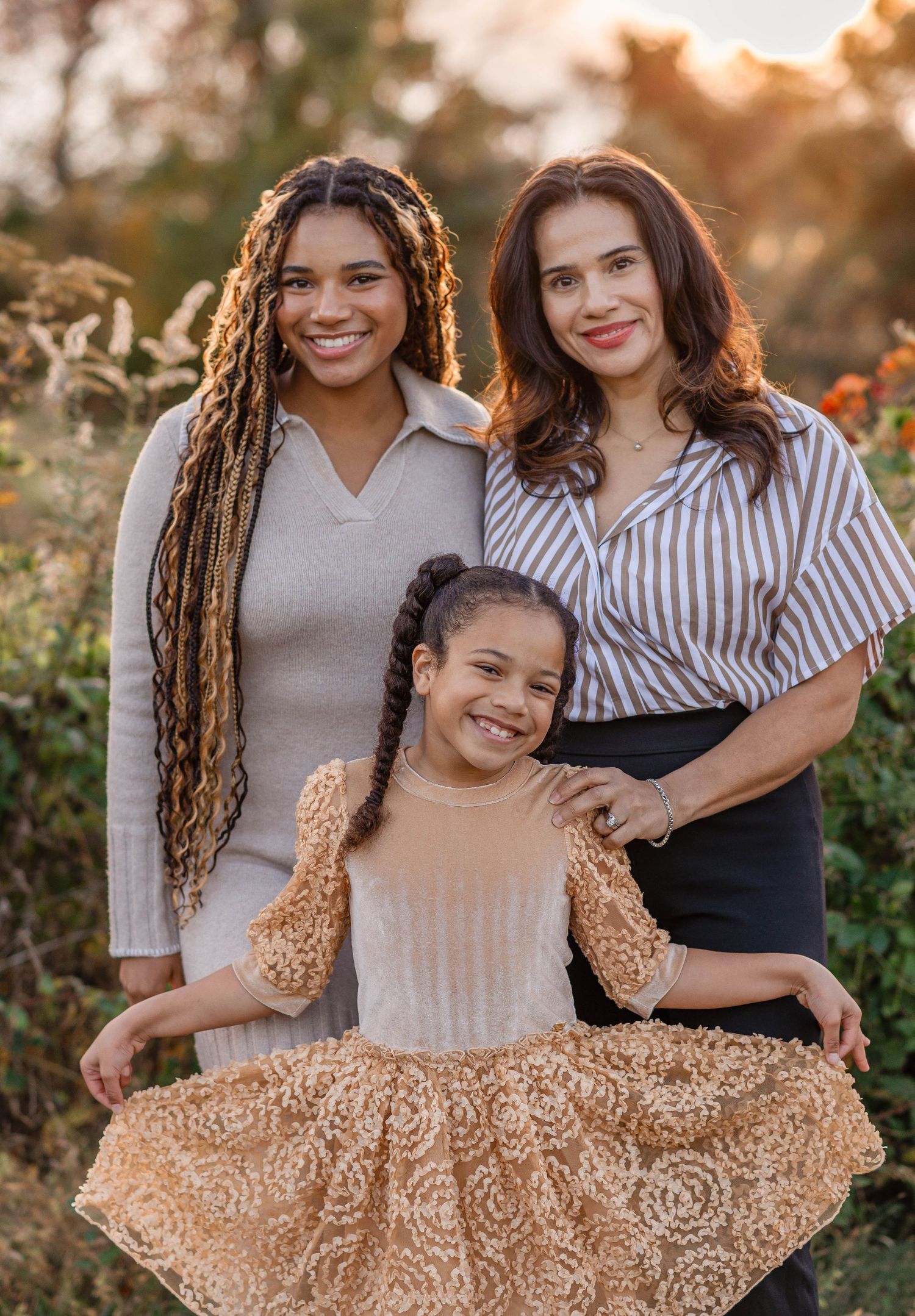A mother poses with her two daughters in a sun-drenched autumn garden during golden hour.