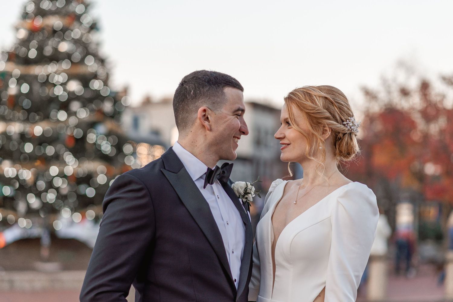 Bride and groom share a romantic moment in front of a decorated Christmas tree at their winter wedding.