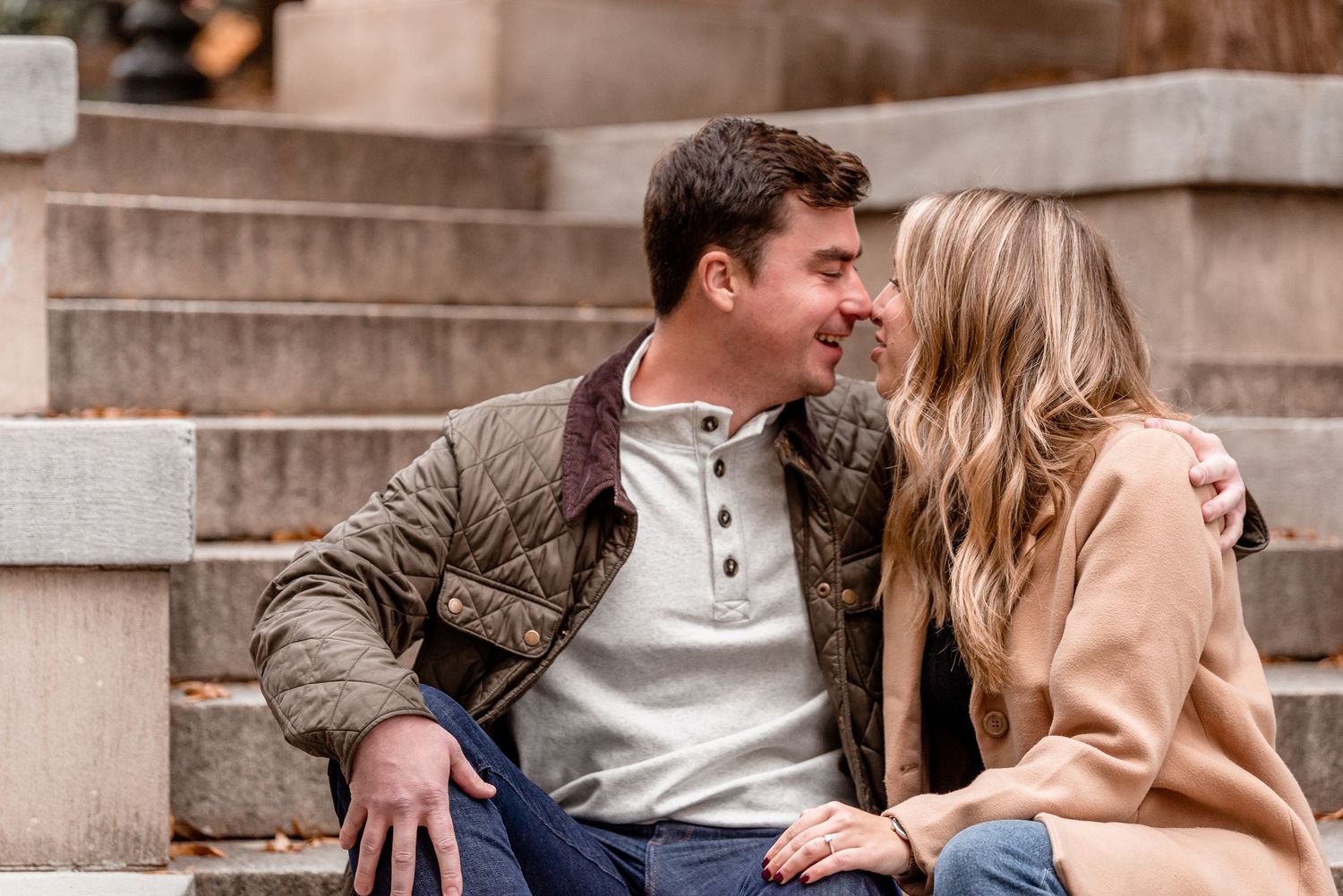 Couple sitting close together on stone steps, smiling and leaning in for a kiss outdoors.