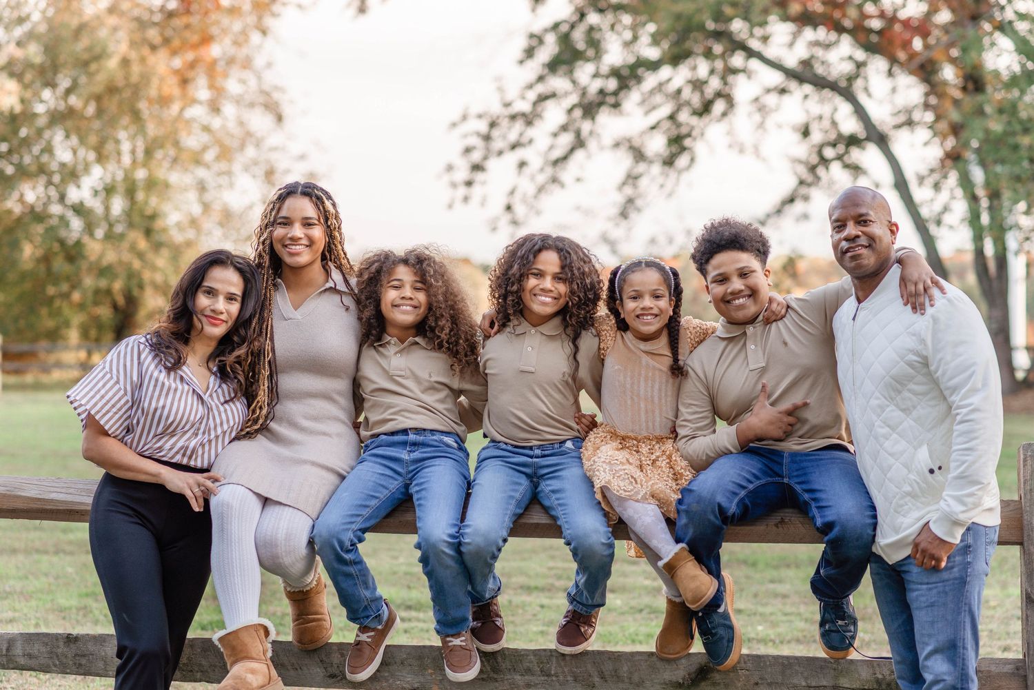 A joyful family of seven poses together on a fence rail surrounded by autumn foliage.