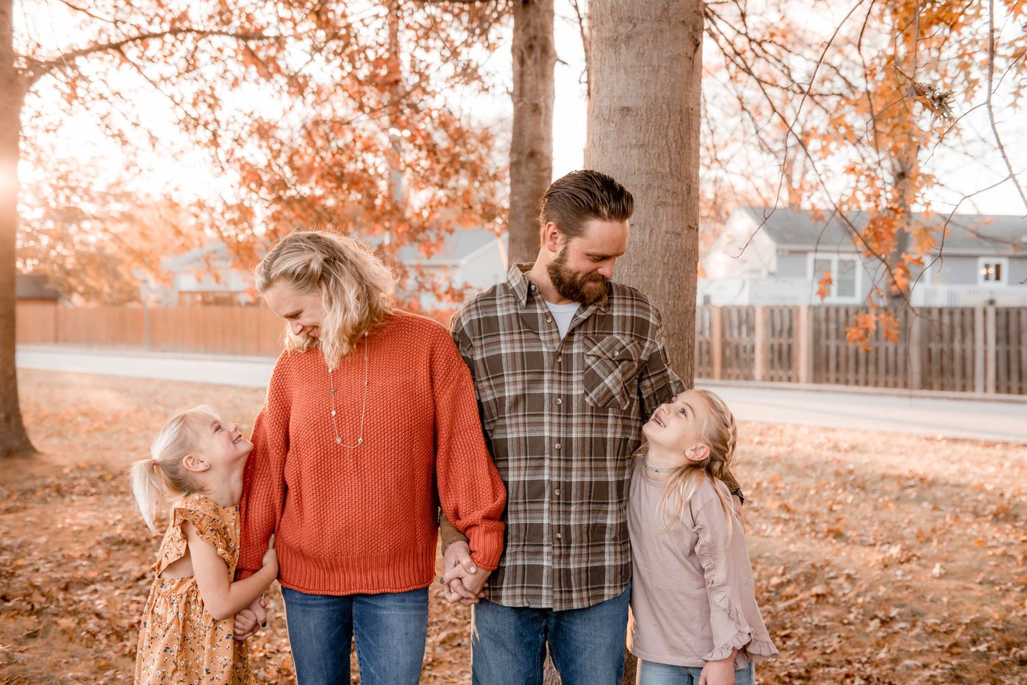 A loving family of four holds hands and smiles among golden fallen leaves during autumn family portraits.