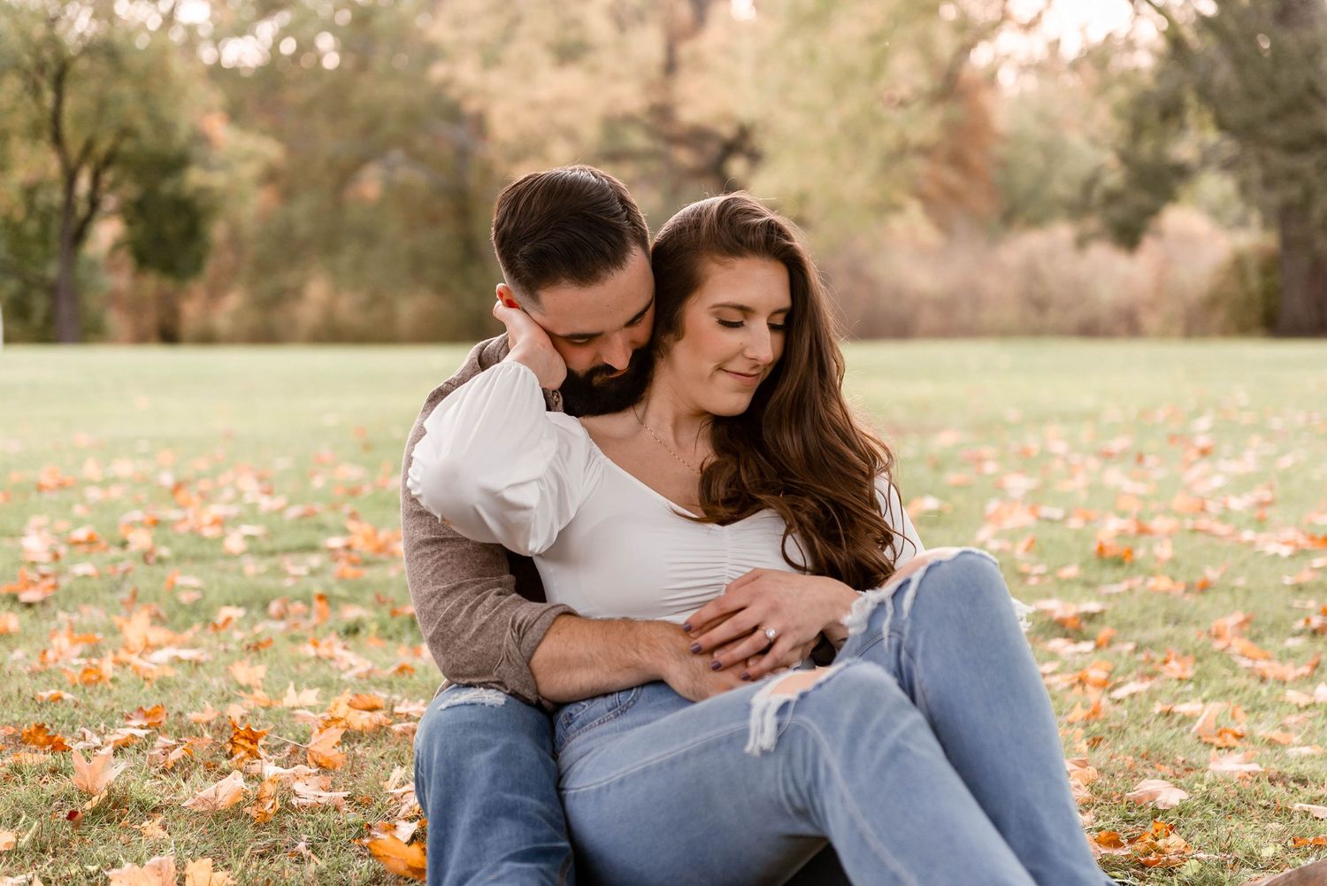 Couple sitting together on autumn grass, sharing an intimate embrace during a fall engagement session.