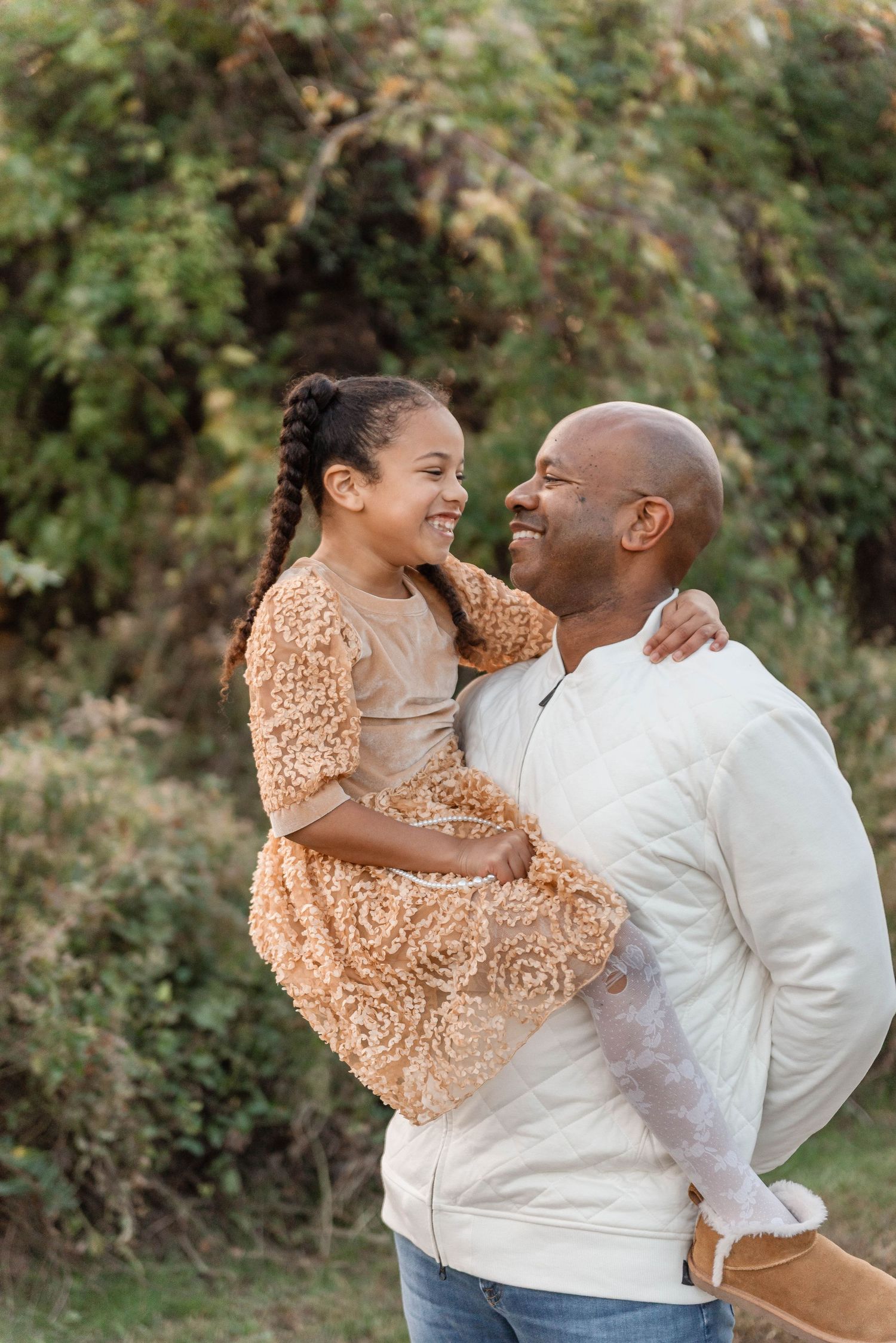 Smiling father holding his young daughter in a floral dress outdoors in nature.