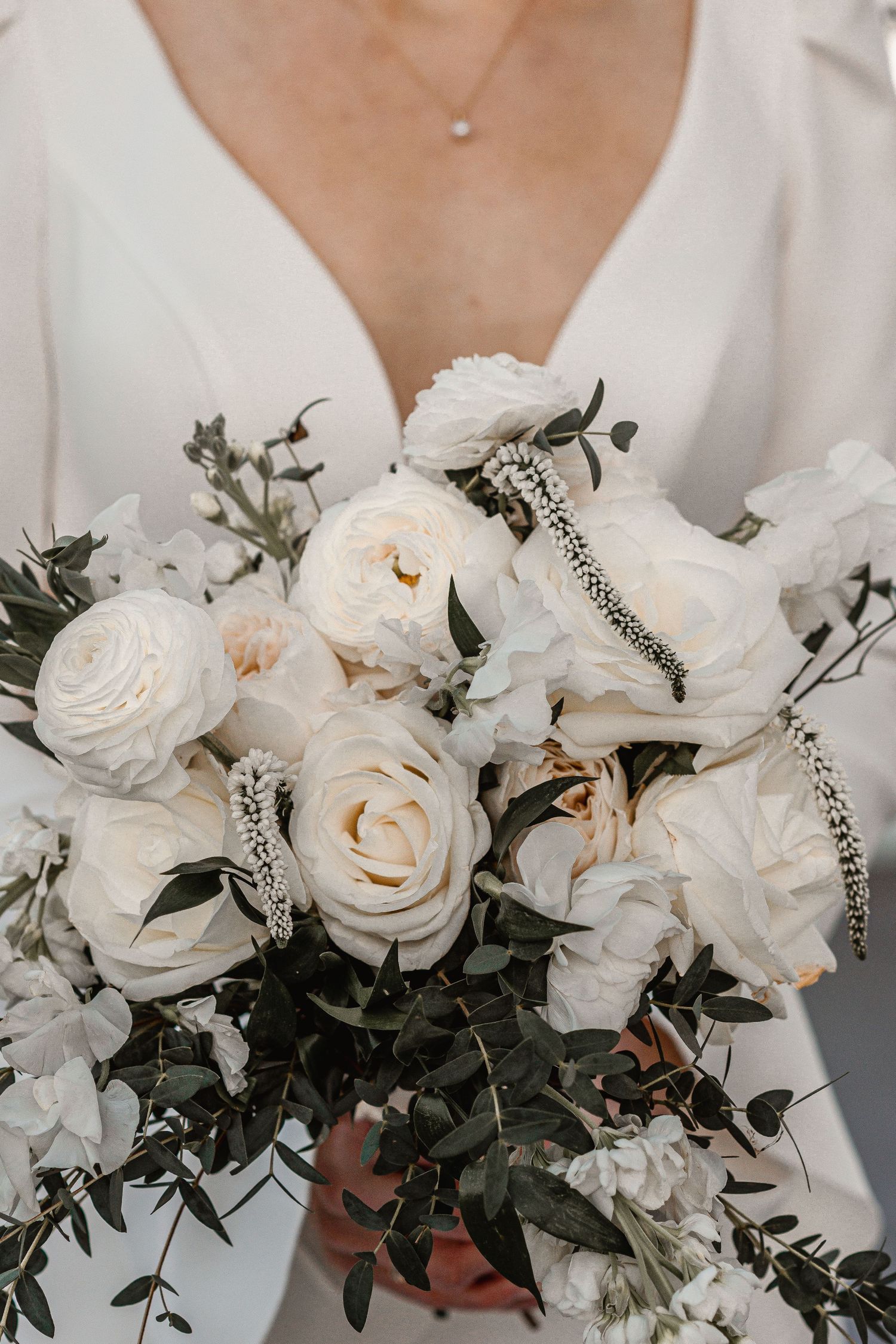 Close-up of bridal bouquet featuring white garden roses, peonies, and greenery with crystal hair pins.