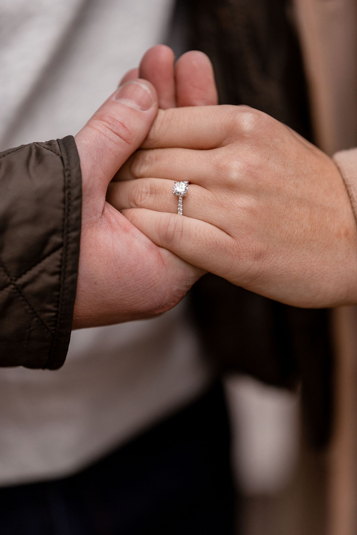 Close-up of a womans hand displaying a diamond solitaire engagement ring held by her partner.