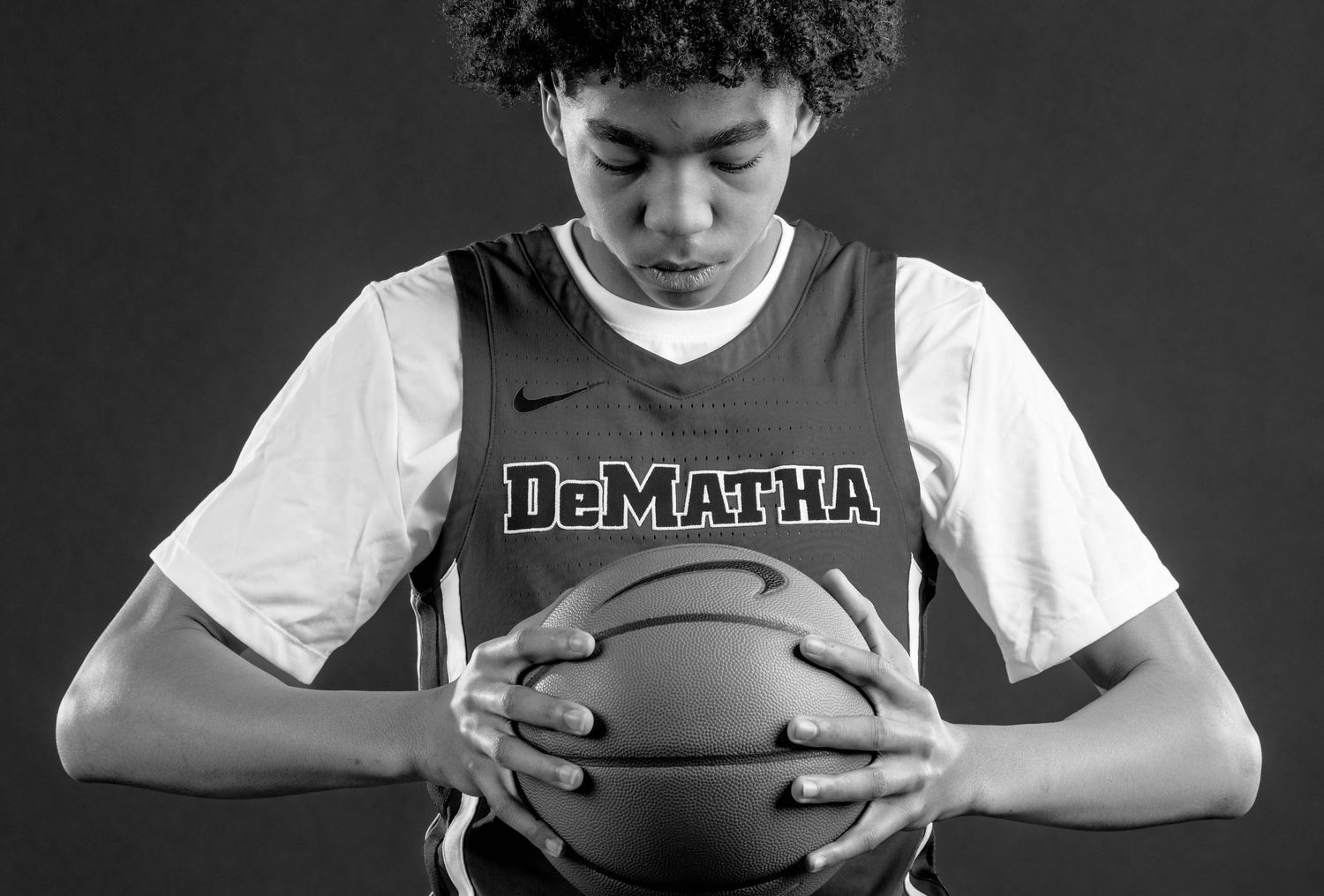 Black and white portrait of teen basketball player holding ball, wearing DeMatha jersey.