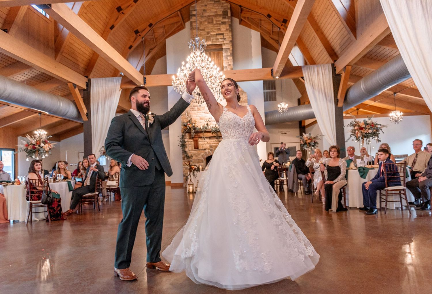 A bride and groom share their first dance under sparkling lights in a rustic wood-beamed wedding venue.