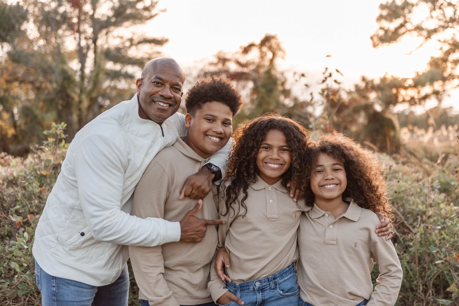 Father posing with his three children in neutral tones during an outdoor fall photoshoot.
