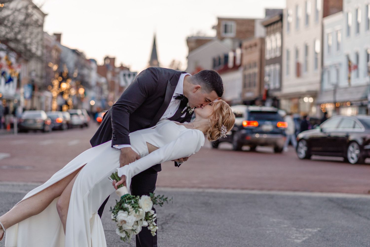 Groom dips bride for a romantic kiss on a charming downtown street during their wedding day.
