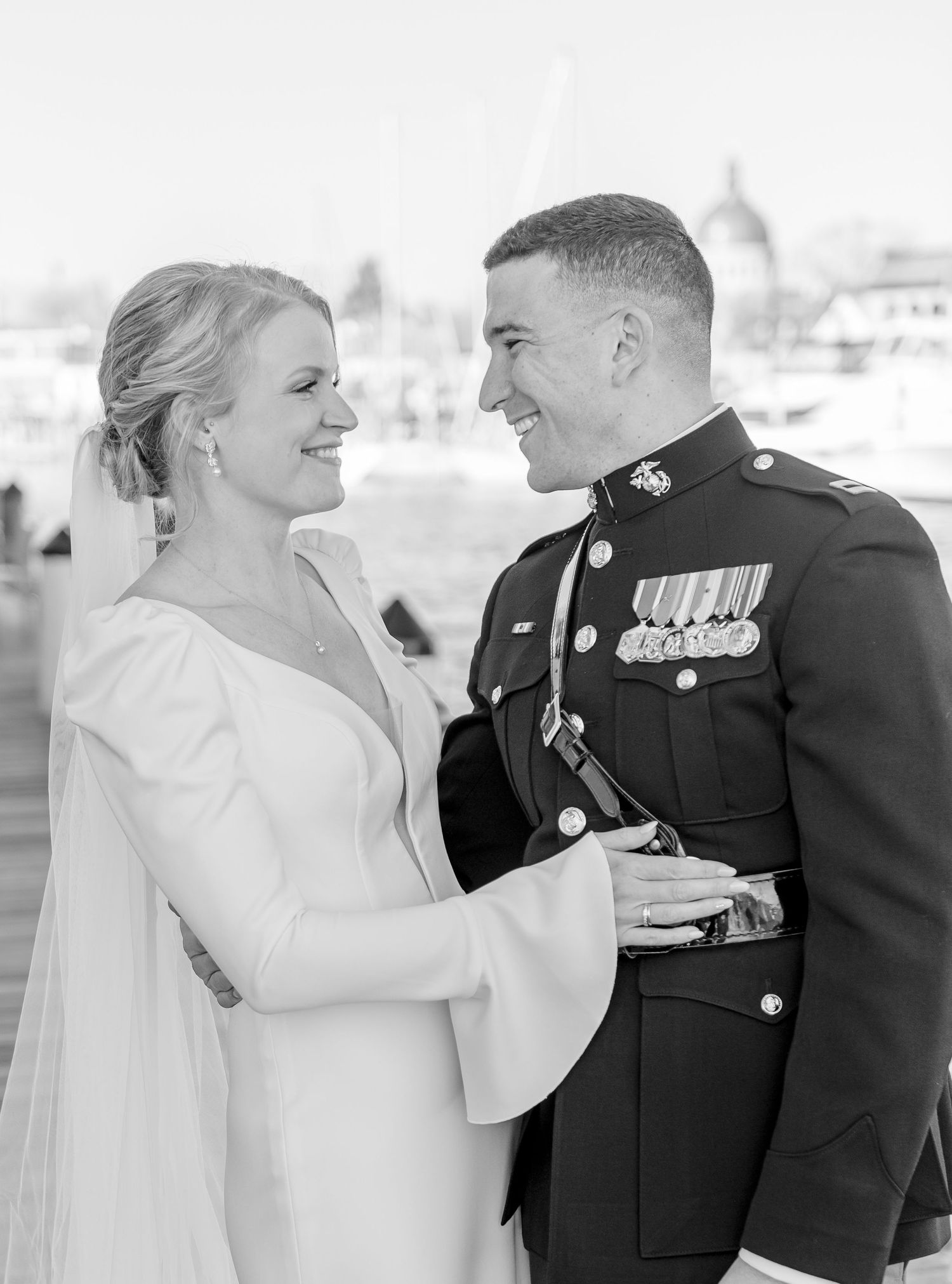 Black and white portrait of a smiling bride and Marine groom in dress blues at a waterfront wedding.
