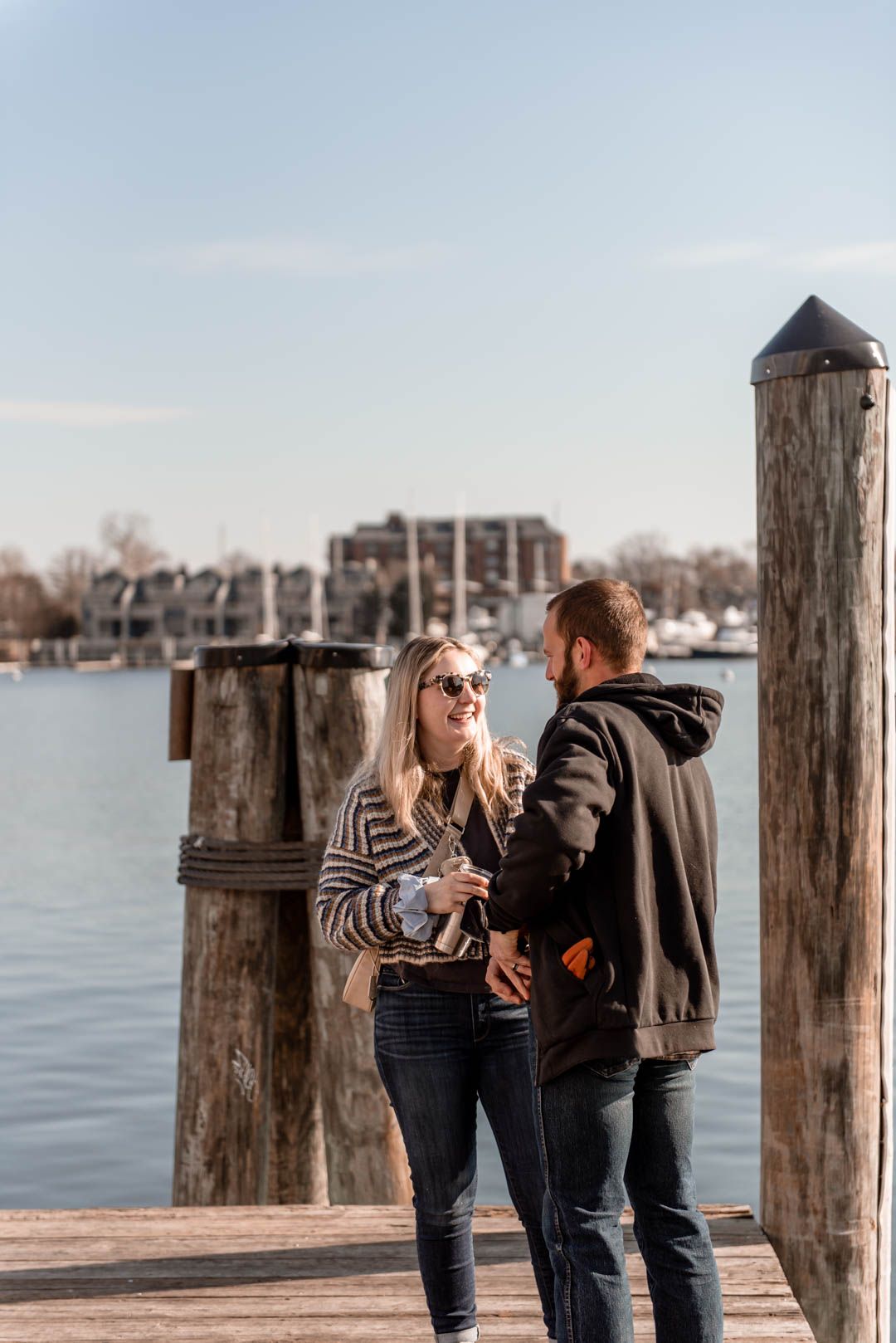 Couple chatting and laughing together on a waterfront dock on a bright sunny day.