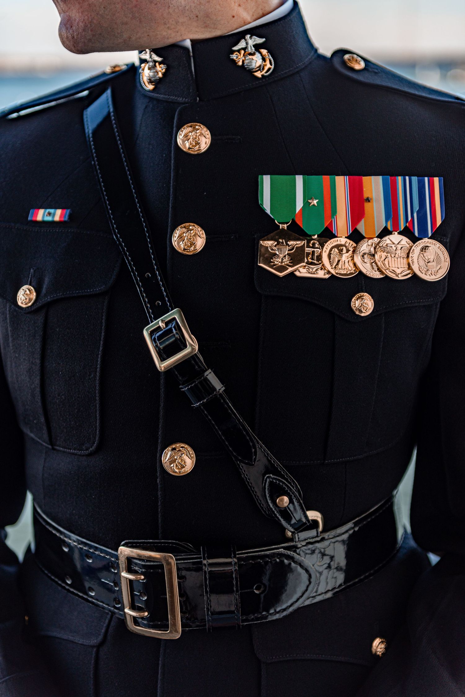 Close-up of a US Marine Corps dress blue uniform adorned with medals, ribbons, and gold buttons.