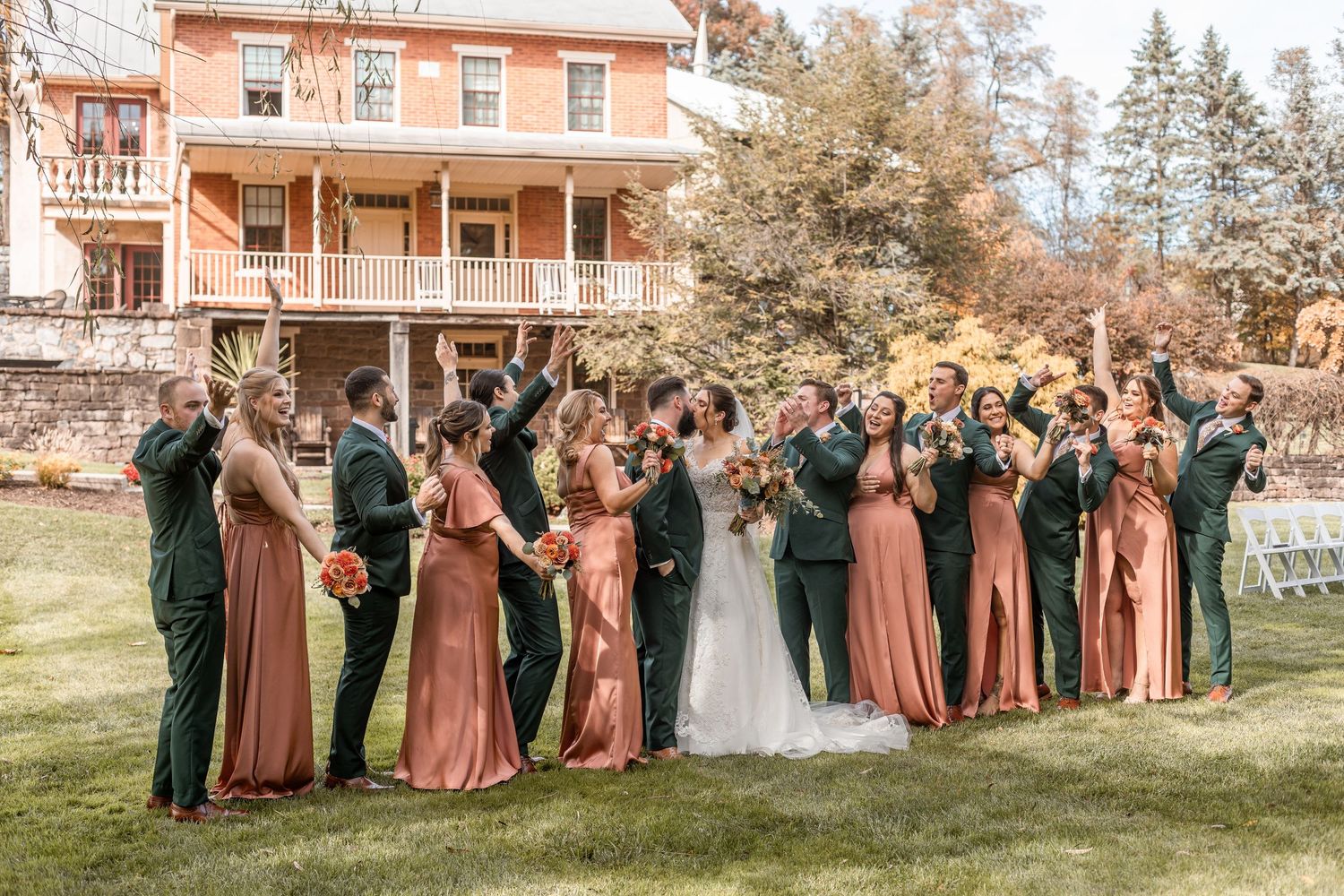 Full wedding party in terracotta and dark green attire celebrating outdoors at fall estate wedding.