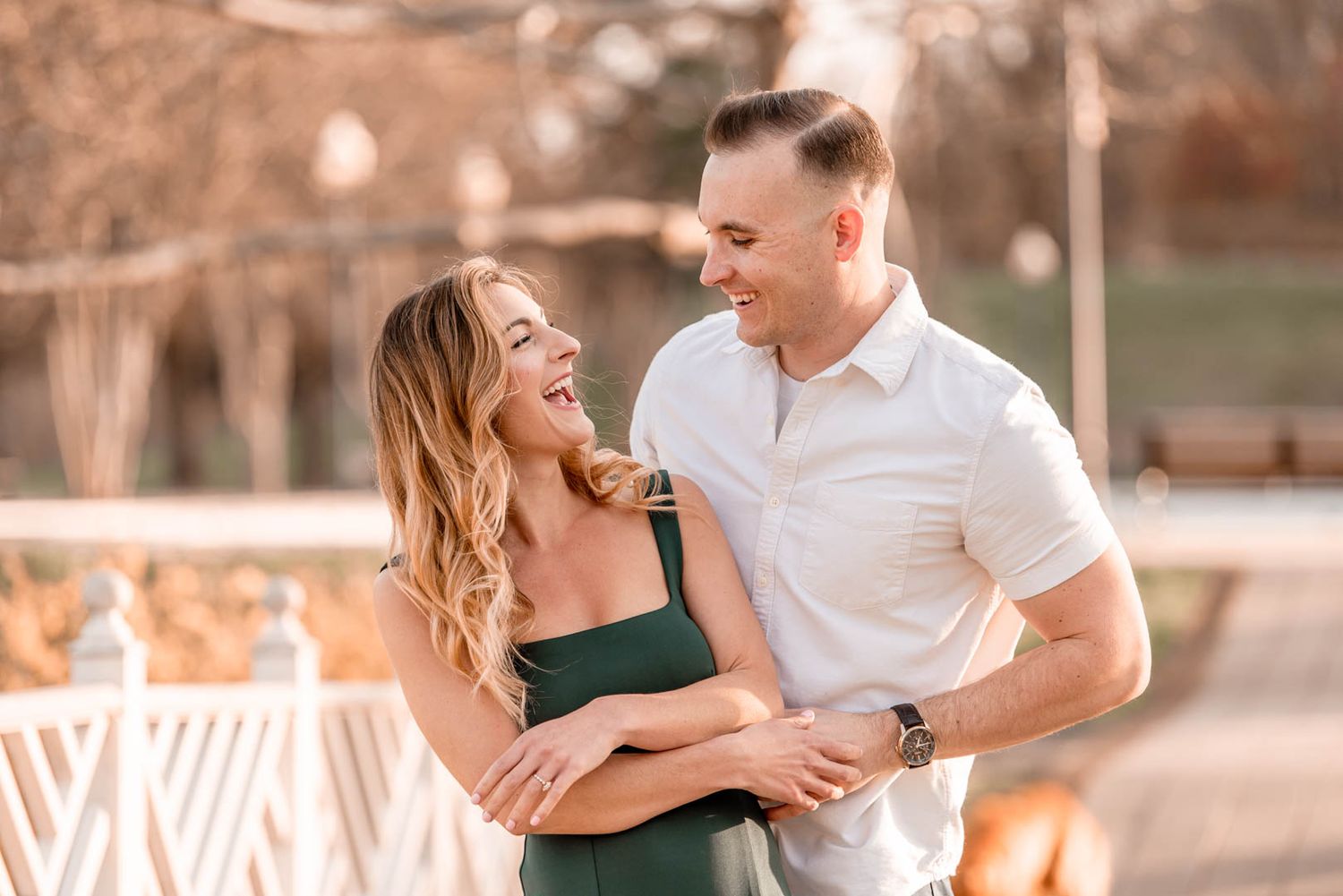 Happy couple laughing and embracing outdoors, woman in green dress and man in white shirt during engagement photos.