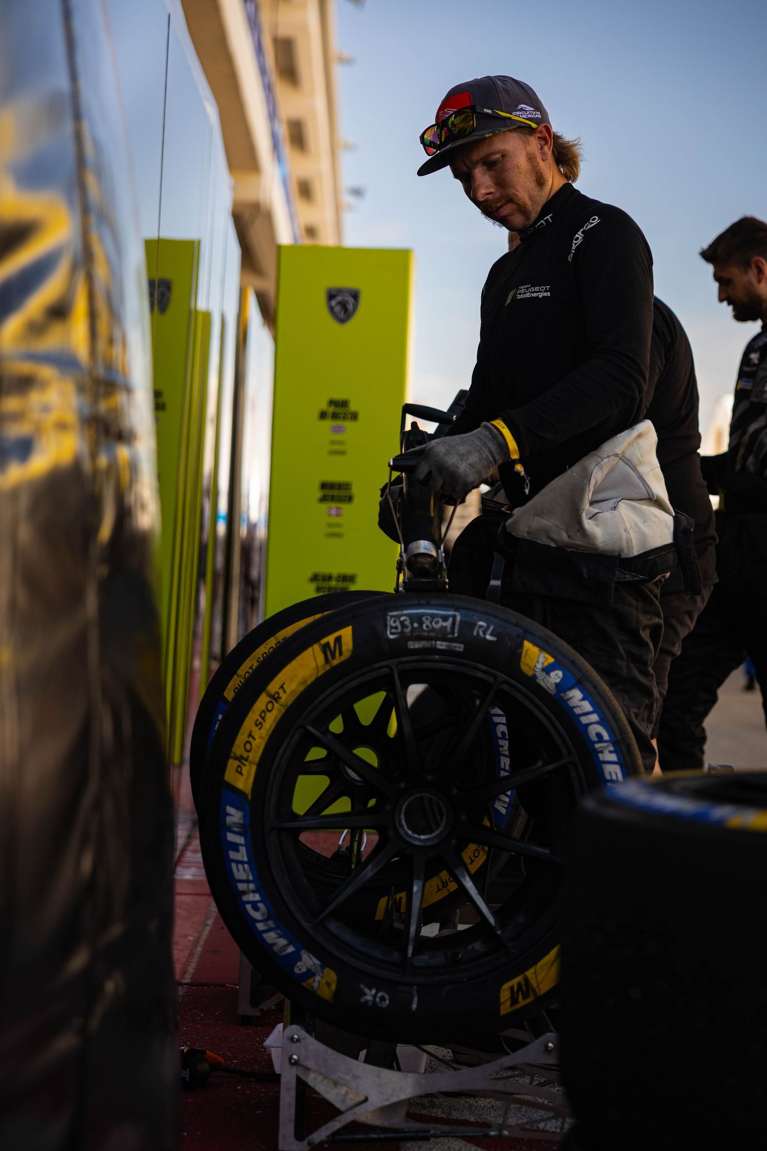 Mechanic handling Michelin racing tires in the pit lane at a motorsport event.