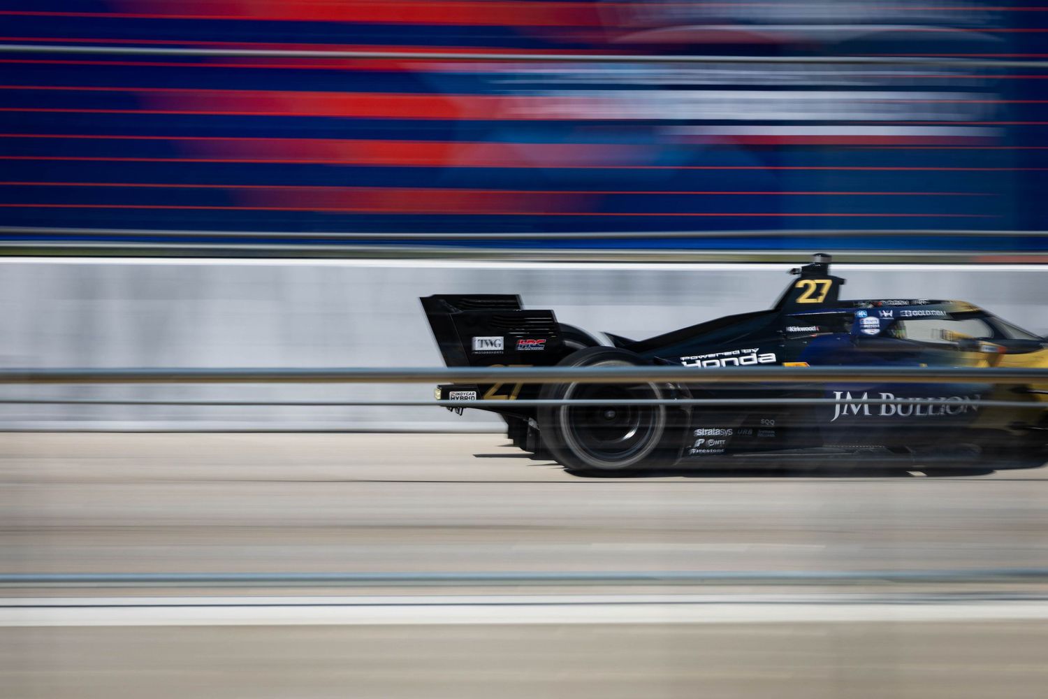 Formula E race car number 27 speeds past with motion blur at a motorsport circuit during competition.