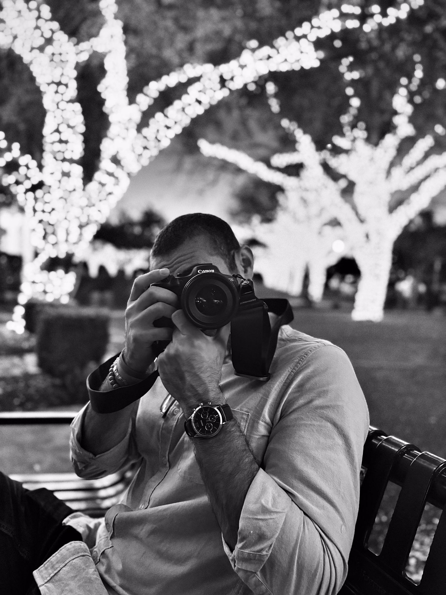 Man photographing with DSLR camera outdoors surrounded by bokeh fairy lights at night.