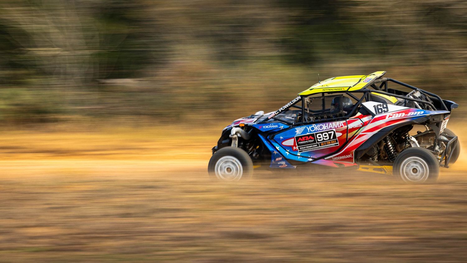American-flag themed UTV racing at high speed across a dusty off-road trail.