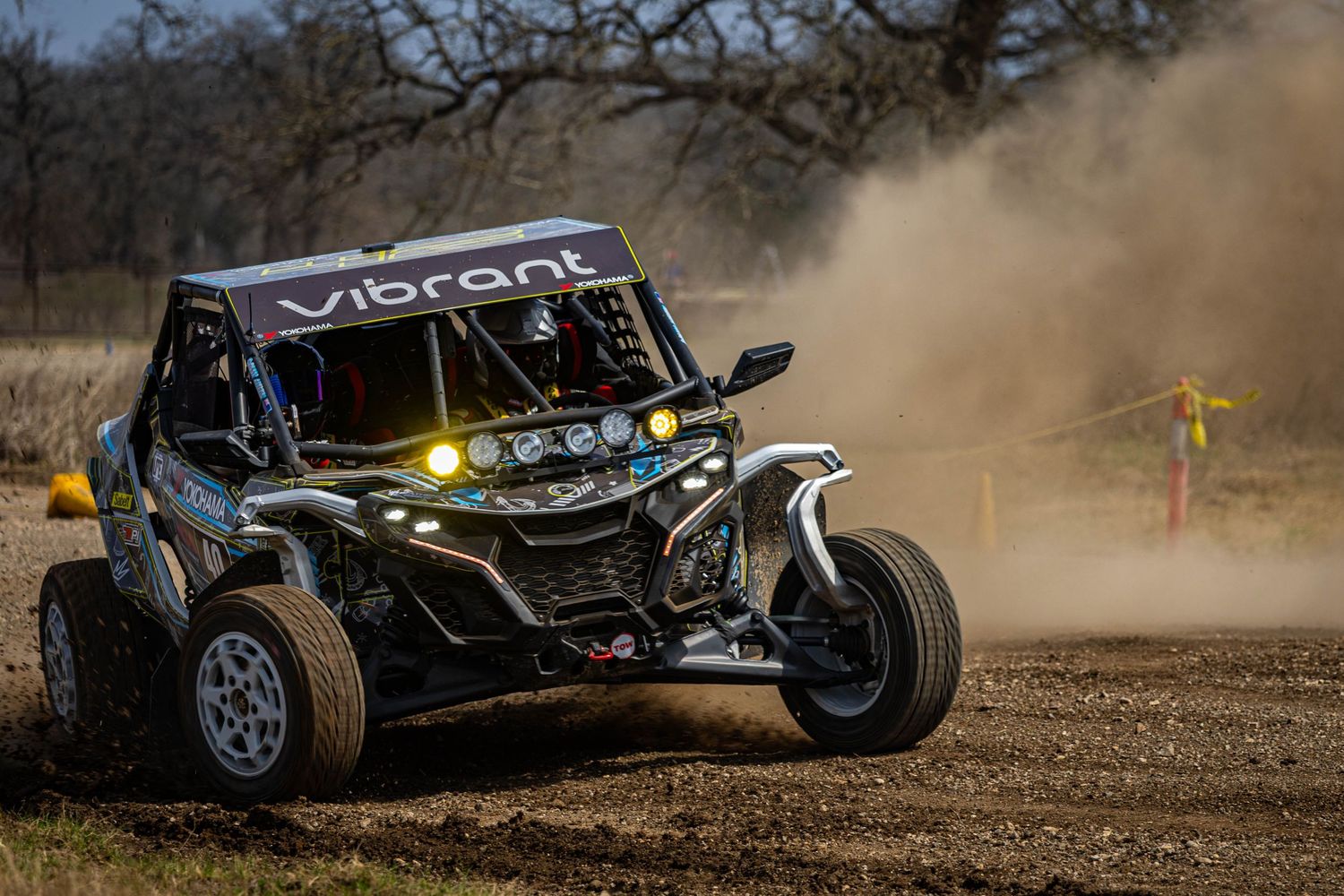 Black Vibrant off-road buggy racing through dusty dirt terrain with headlights on.