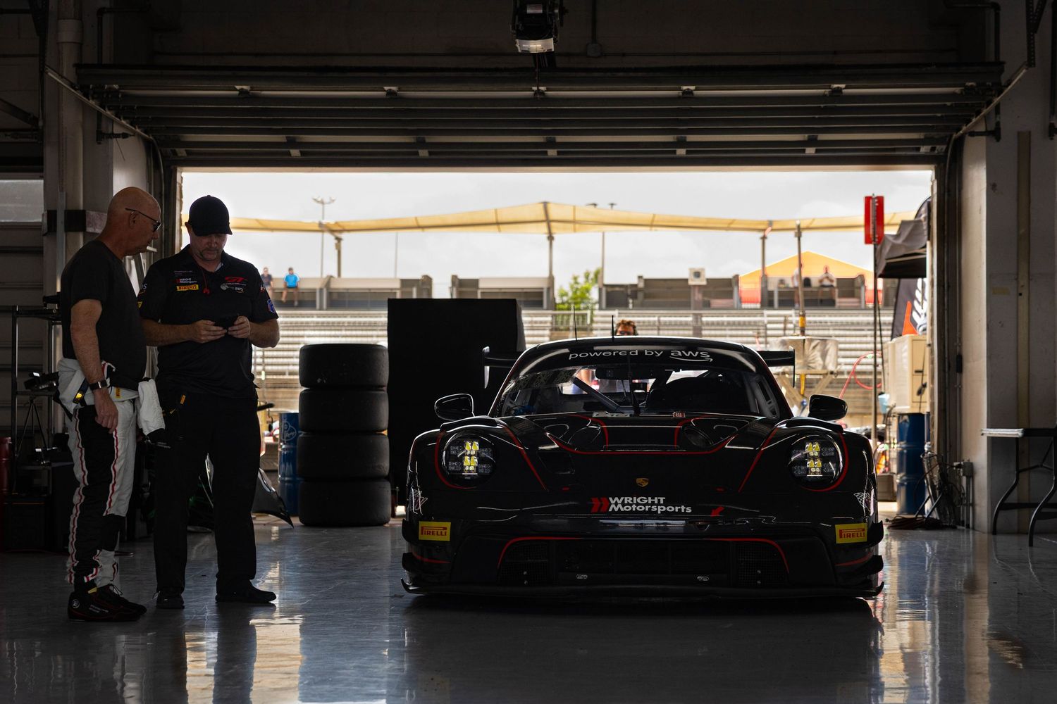 Black GT race car in a dimly lit garage with two crew members reviewing data.